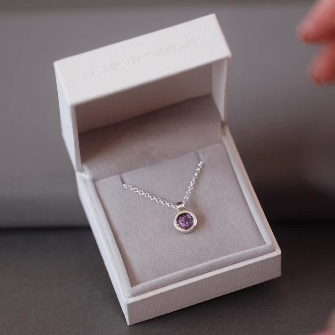 Silver ashes small round pendant necklace with purple crystals in a grey jewellery box held in a women's hand.