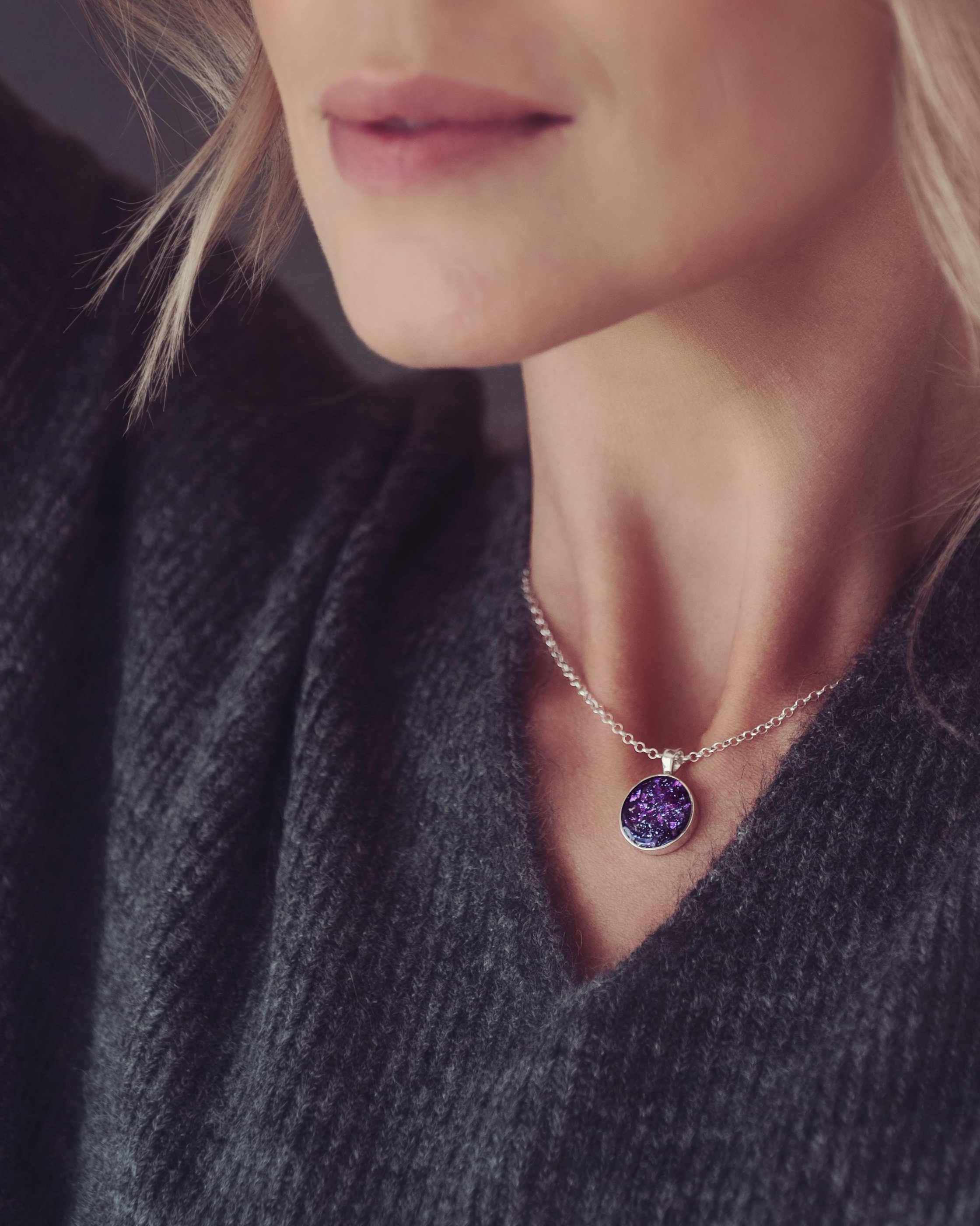 a round purple necklace filled with cremation ashes worn on a lady with blond wavy hair