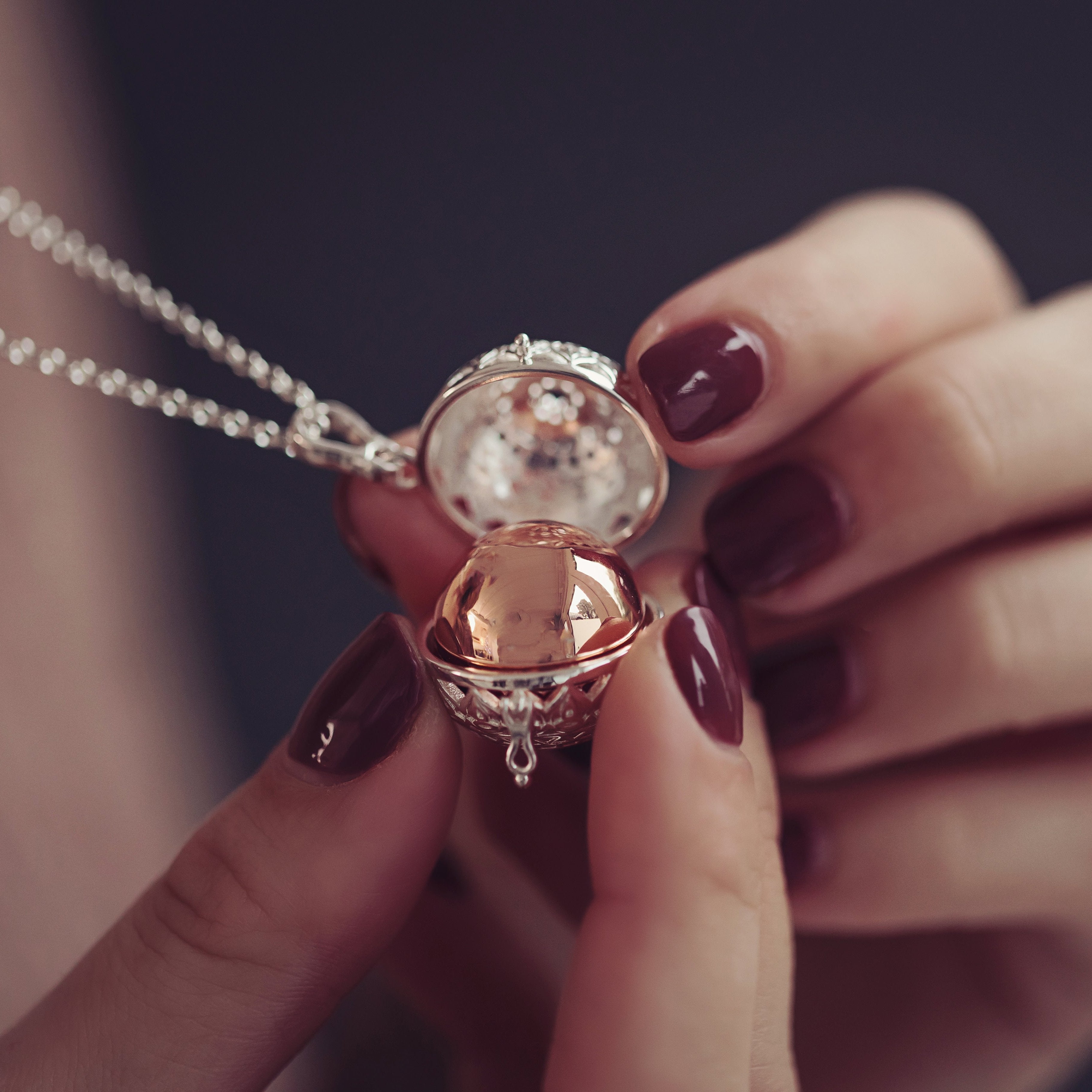 A woman delicately holding a self-fill locket necklace with a rose gold sphere containing cremation ashes