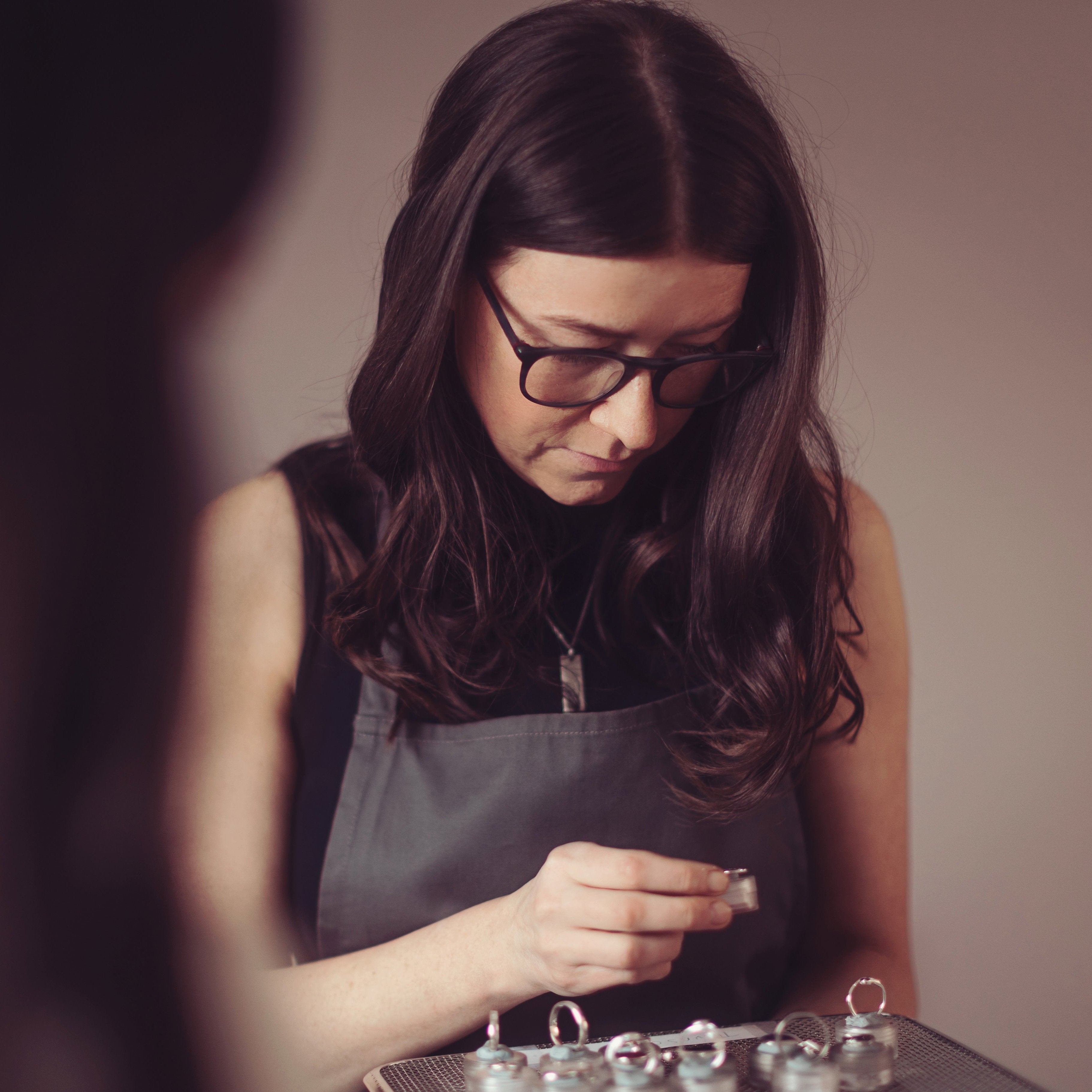 A woman with long dark hair and glasses inspecting cremation ashes rings on a tray