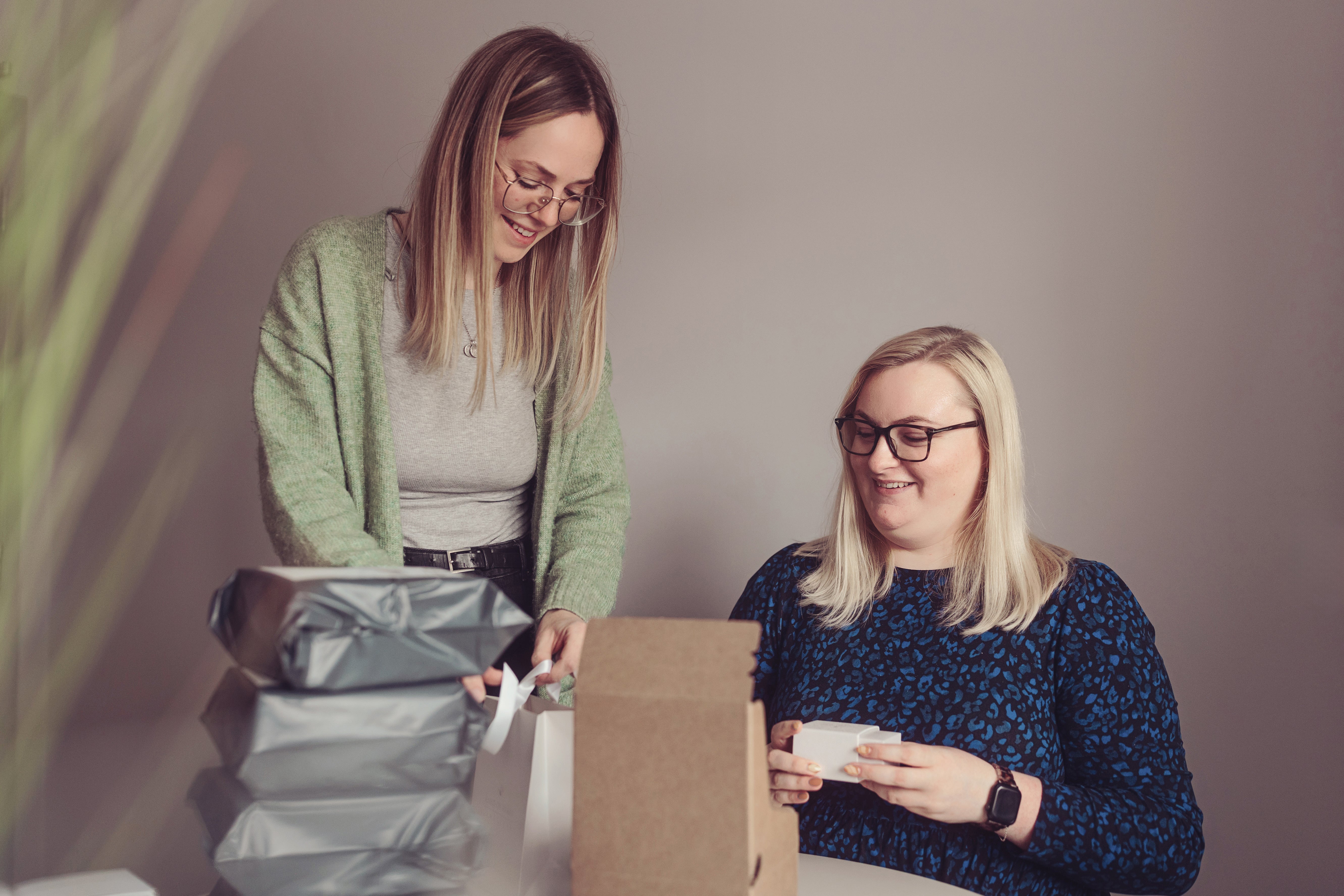 Two team members smiling and packing orders at a table, surrounded by wrapped packages