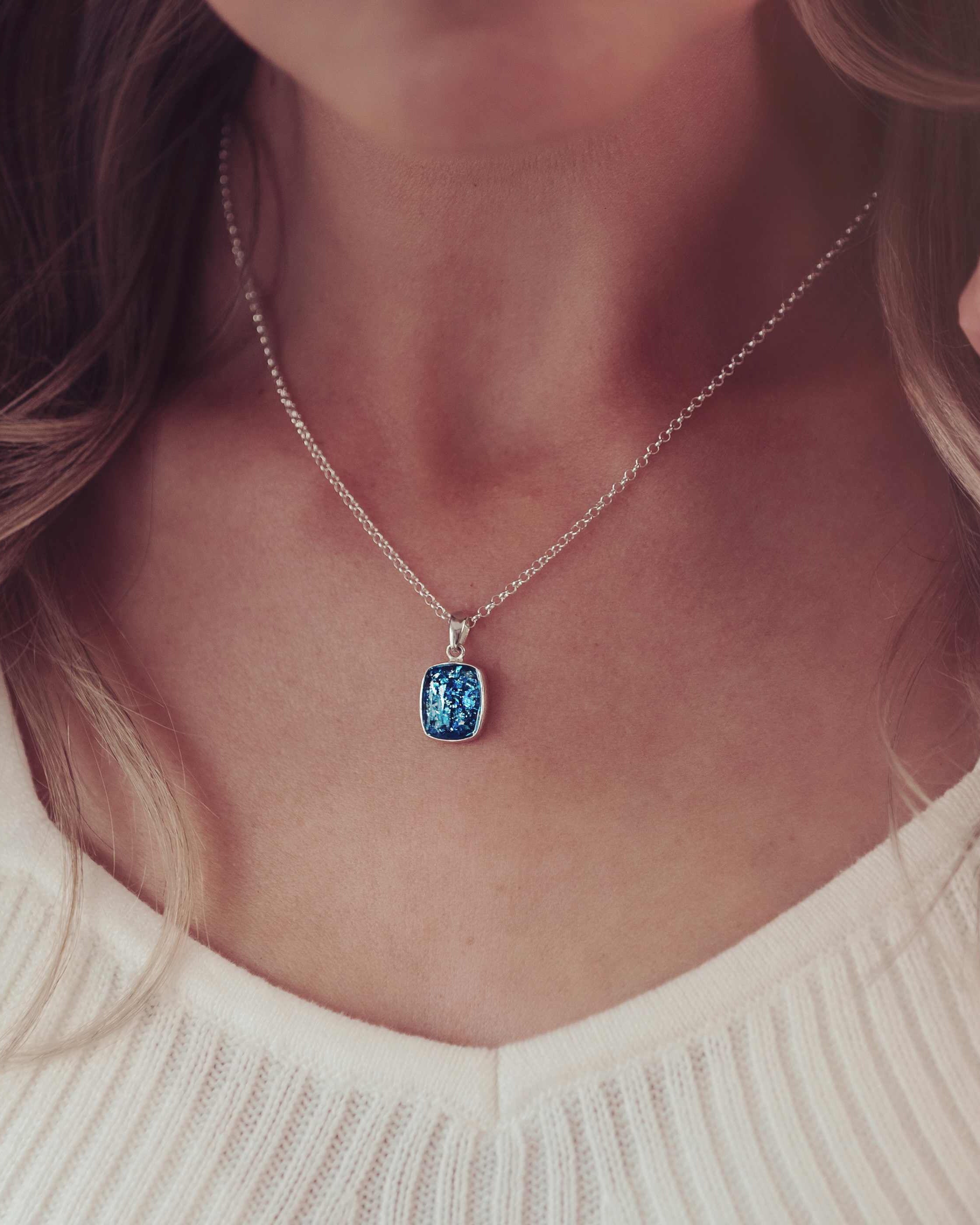 imaged focussed on a lady's neck with a square blue necklace filled with cremation ashes