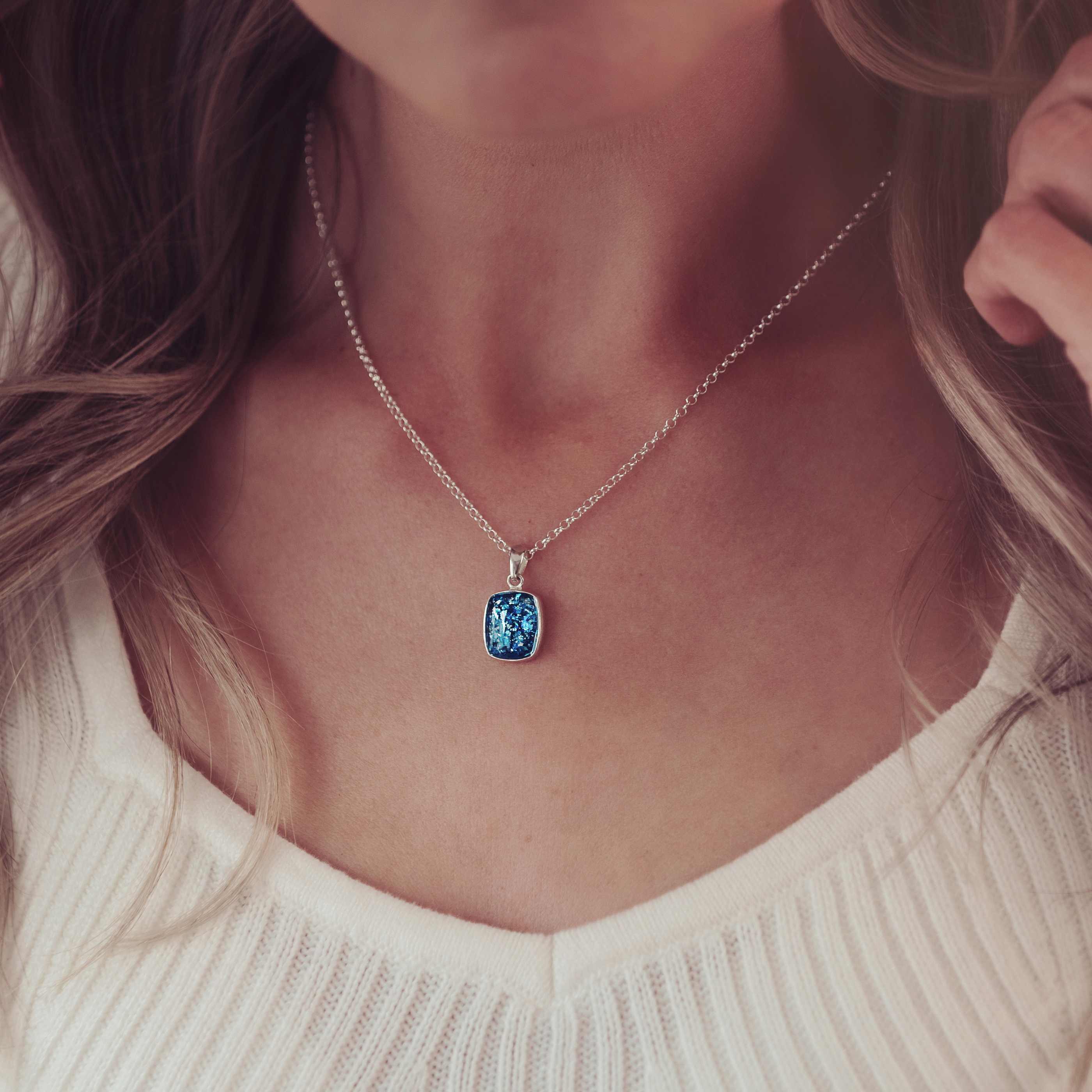imaged focussed on a lady's neck with a square blue necklace filled with cremation ashes