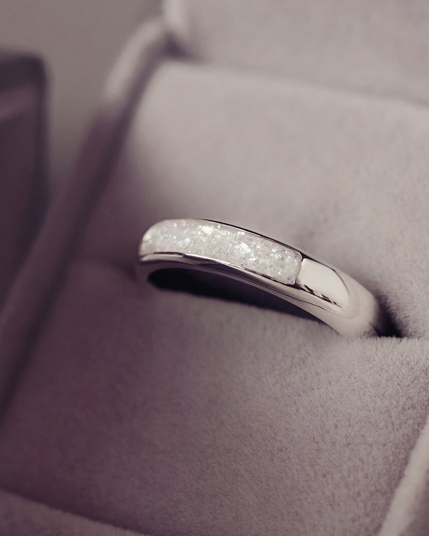 Sterling silver womens ring band with a central section filled with  memorial ashes and clear crushed crystals, displayed in a grey jewellery box