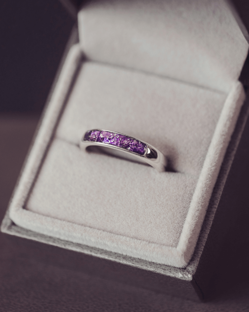 Sterling silver womens ring band with a central section filled with  memorial ashes and purple crushed crystals, displayed in a grey jewellery box