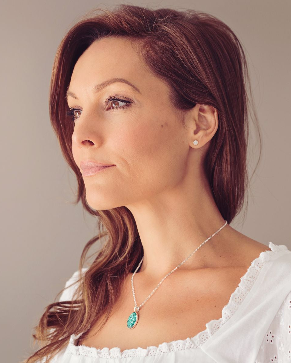 side profile of a brunette last in a white lace top wearing a Sterling silver oval necklace with a central section filled with memorial ashes and green crushed crystals