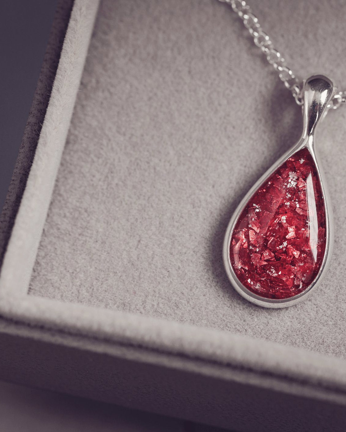 Sterling silver teardrop necklace with a central section filled with memorial ashes and red crushed crystals, displayed in a grey jewellery box