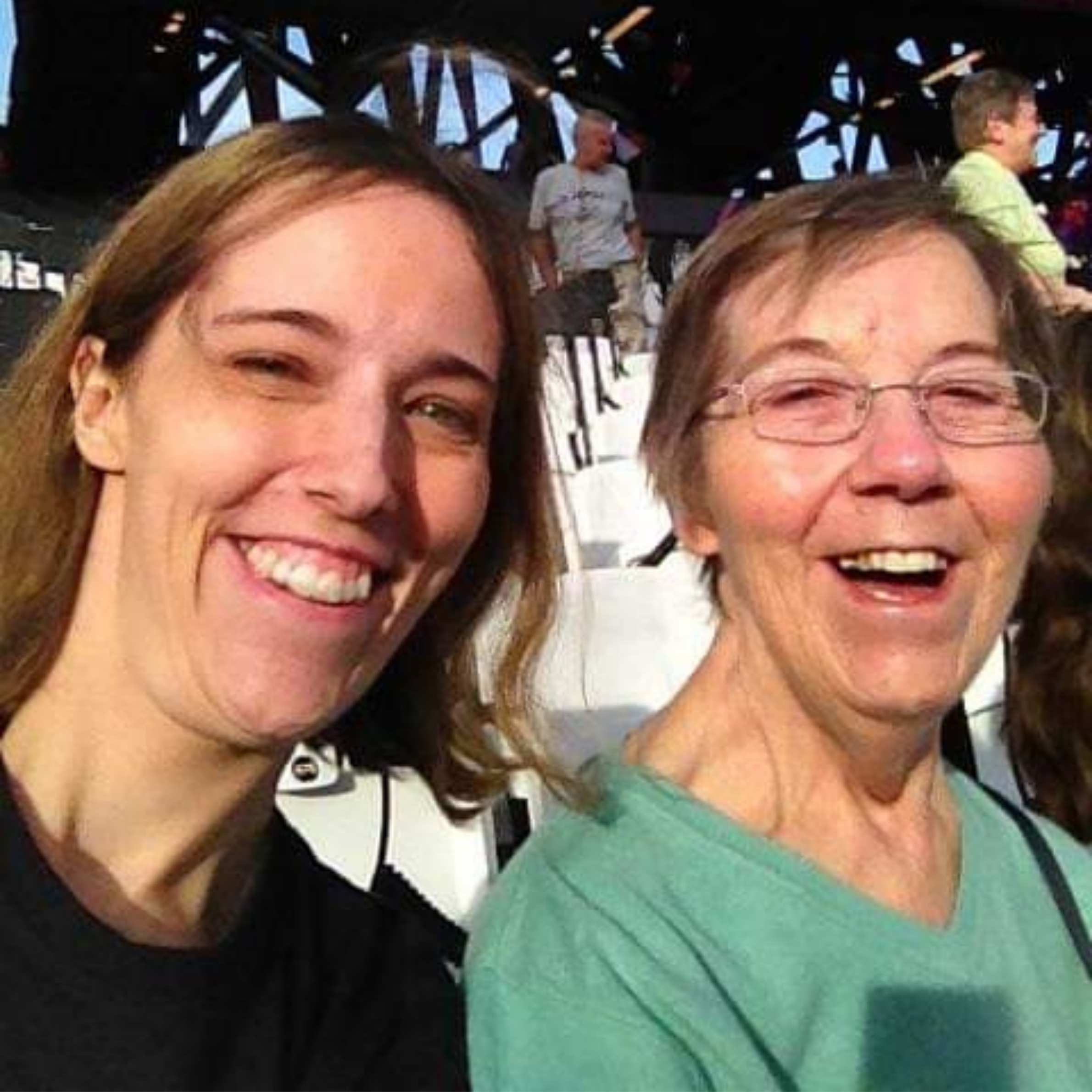 Lady to the left has brown short hair and is wearing a black t-shirt. The lady to the right is wearing a green v-neck tshirt and has short brown hair and glasses. 