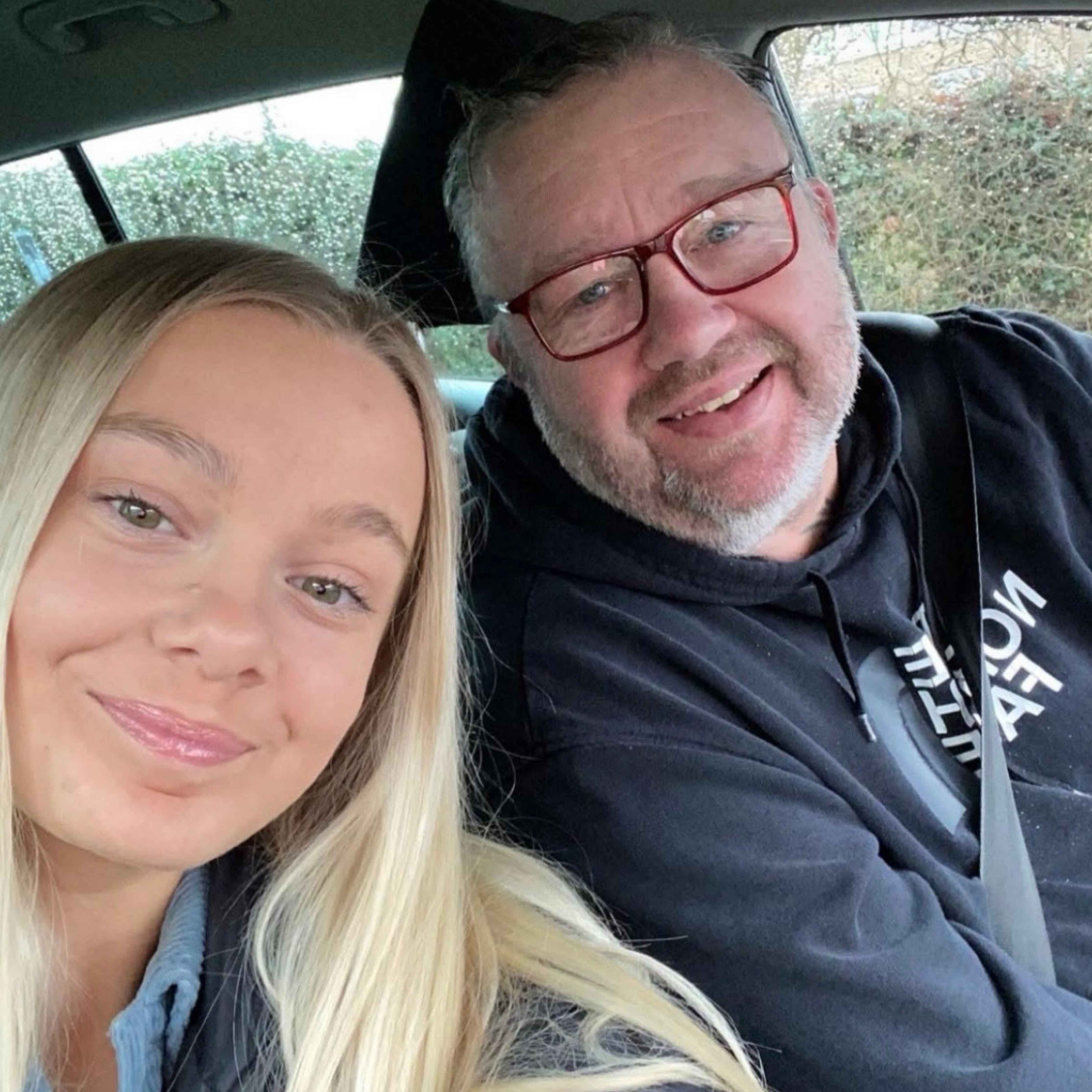 Smiling young woman and older man taking a friendly selfie inside a car, conveying warmth and affection.