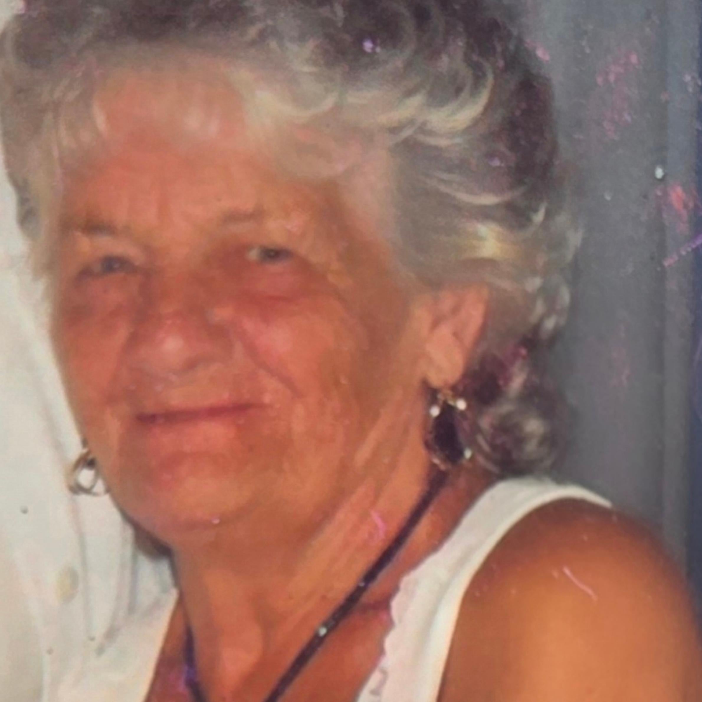 A woman wearing gold earrings, a black necklace and a white top looking towards the camera smiling