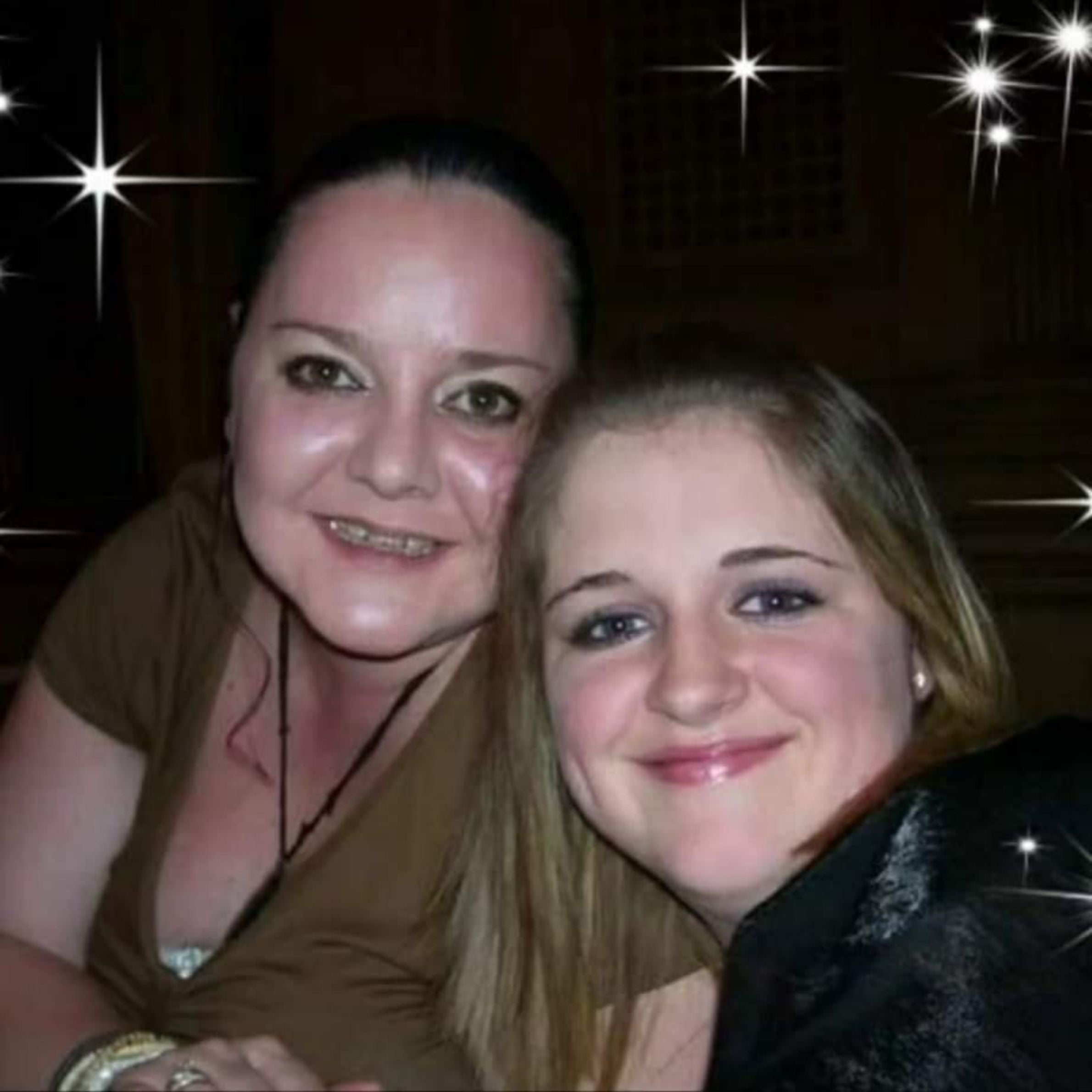 two women smiling for a picture. the woman on the left has dark hair and is wearing a dark green top. the woman on the right has lighter hair and is wearing a black top. there is star affects in the background of the photo