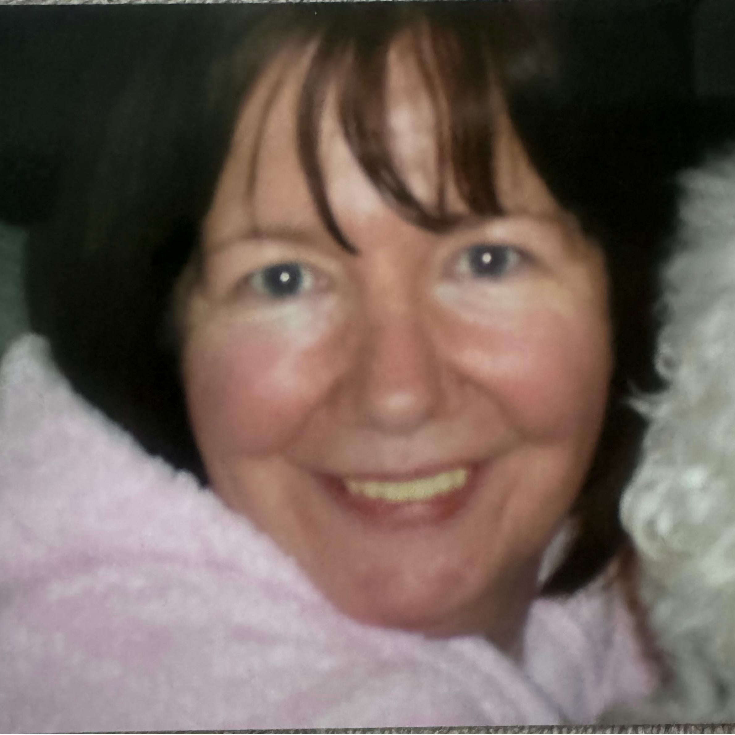 woman with short black hair smiling. shes wearing a pink fluffy top