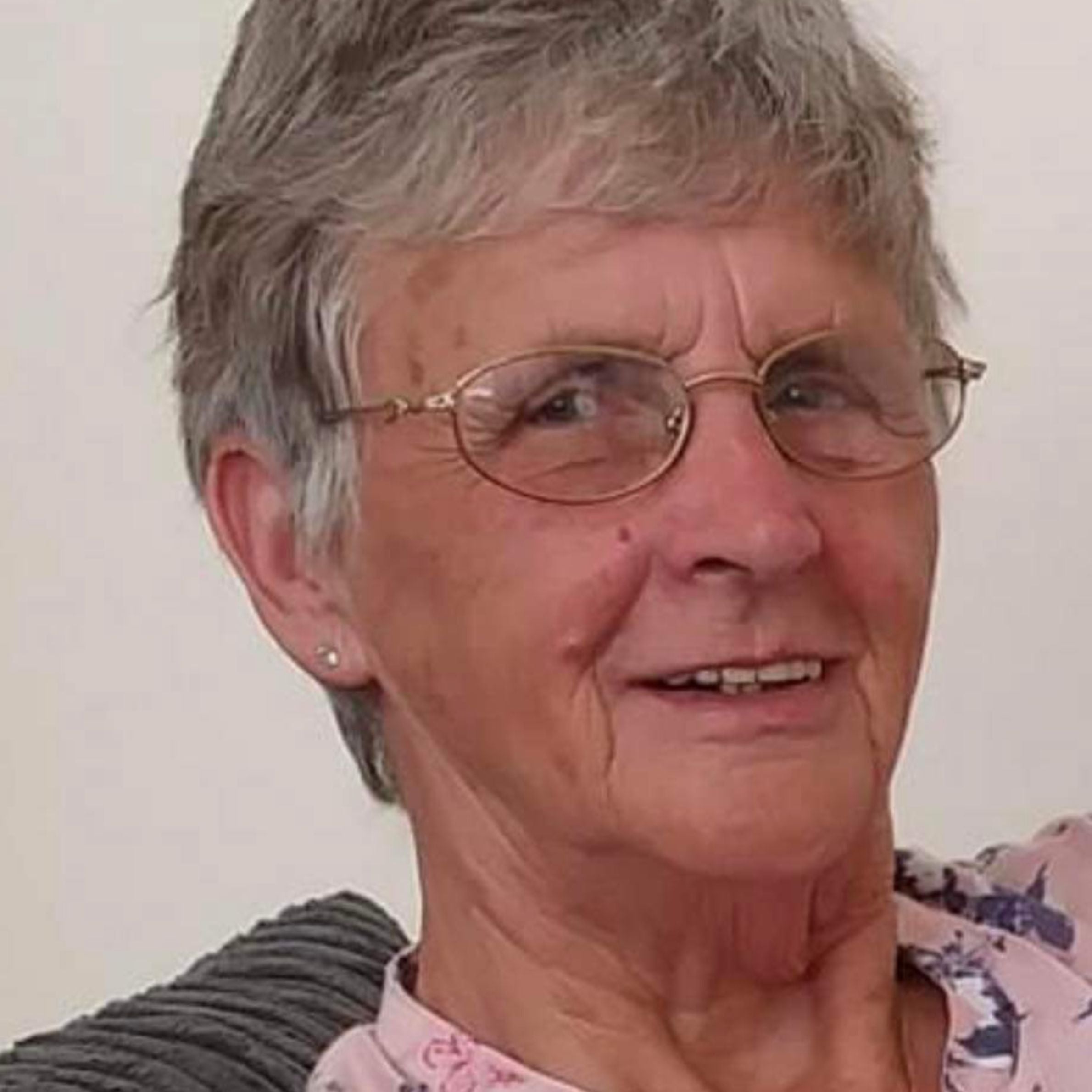 woman with grey short hair wearing glasses and wearing a pink patterned shirt