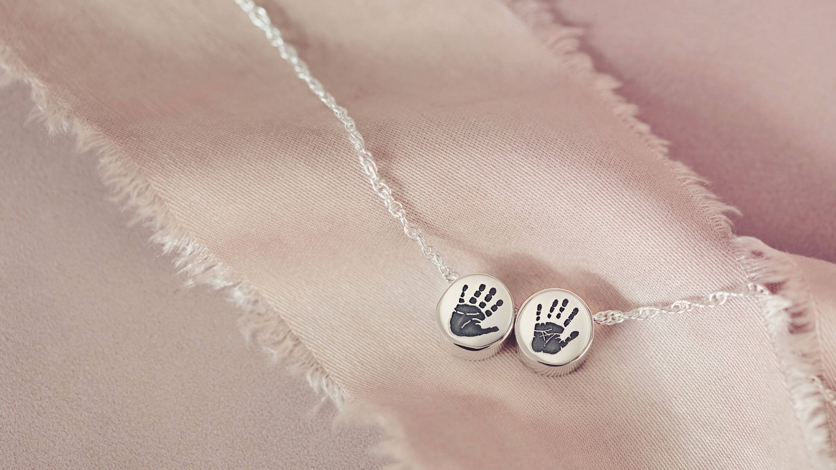 A sterling silver family necklace with two round charm beads, each featuring a handprint