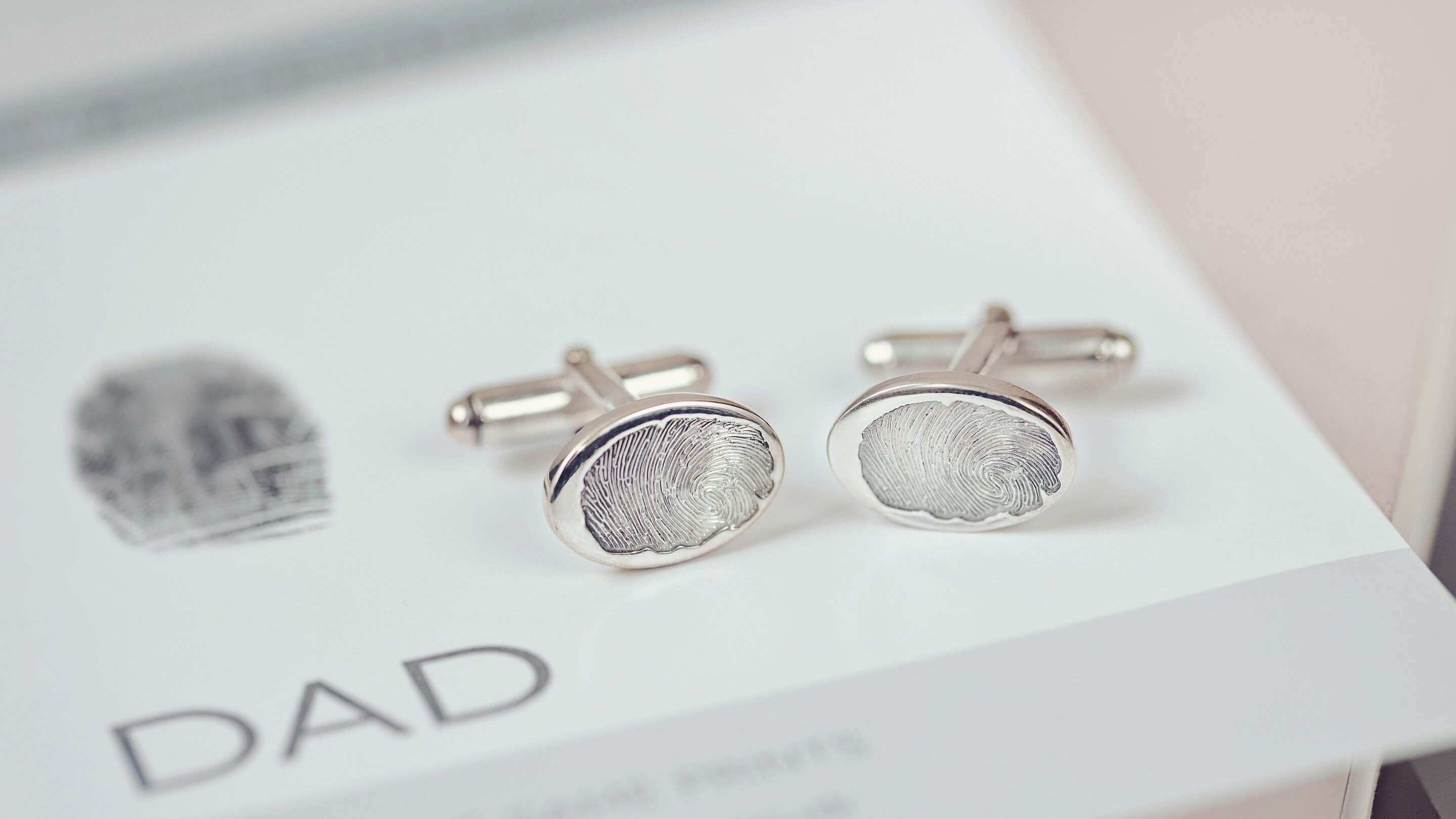 A set of sterling silver cufflinks created with Fingerprints, on a card showing the original fingerprint above the word 'Dad'