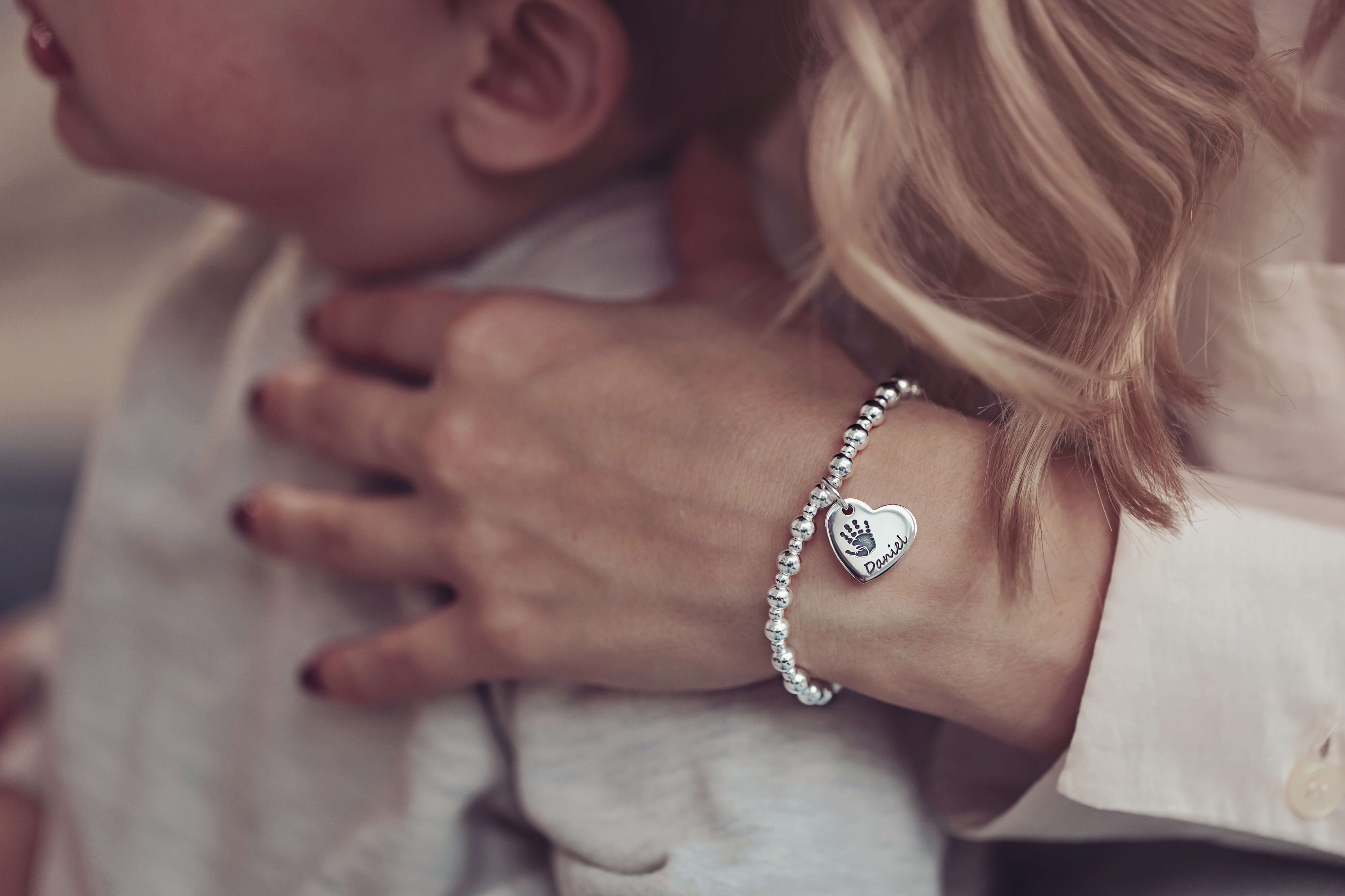 A woman wearing a silver handprint charm bracelet, with her arm around her son