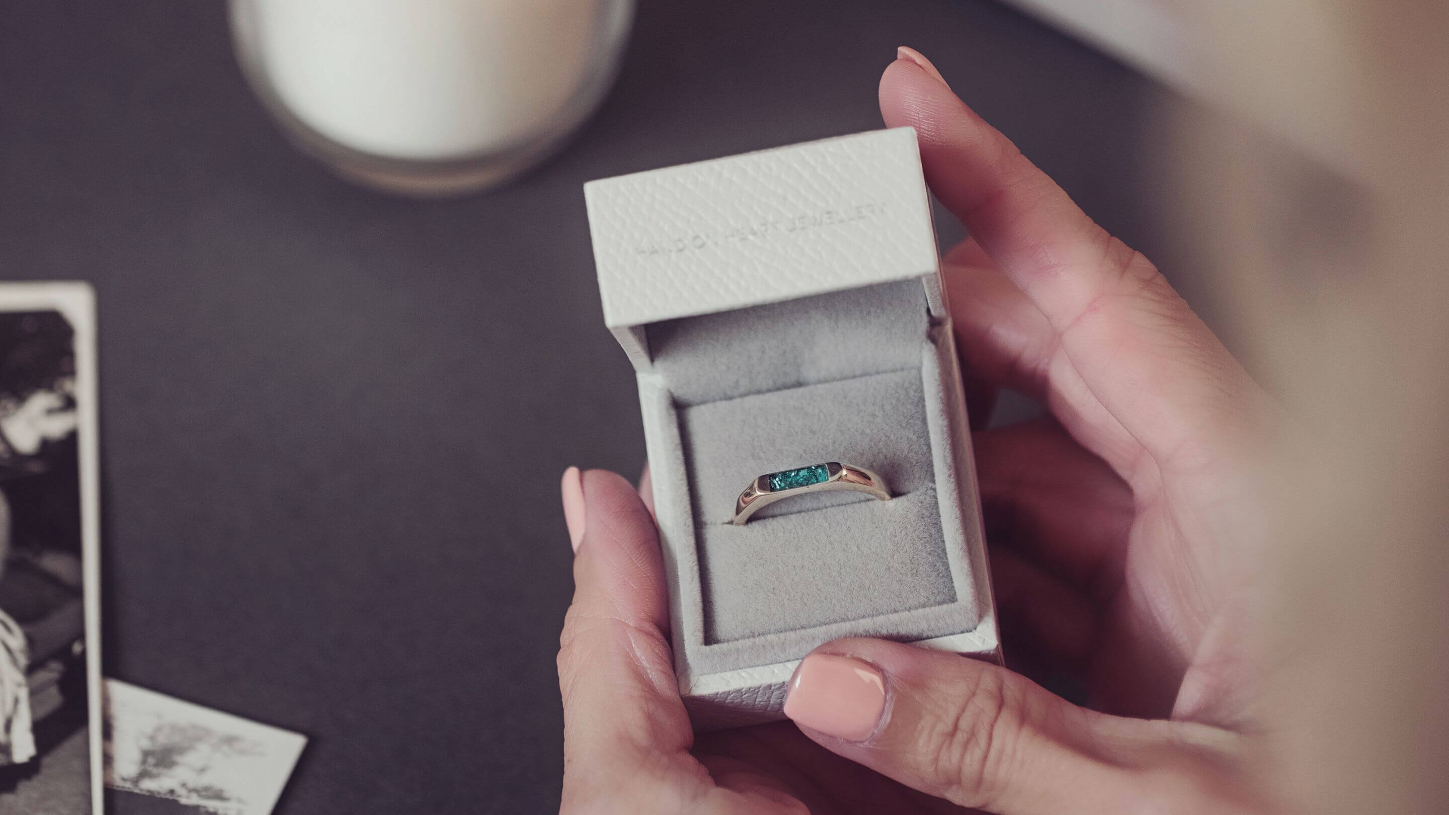 A lady with painted nails holding a jewellery box which contains a gold cremation ashes ring