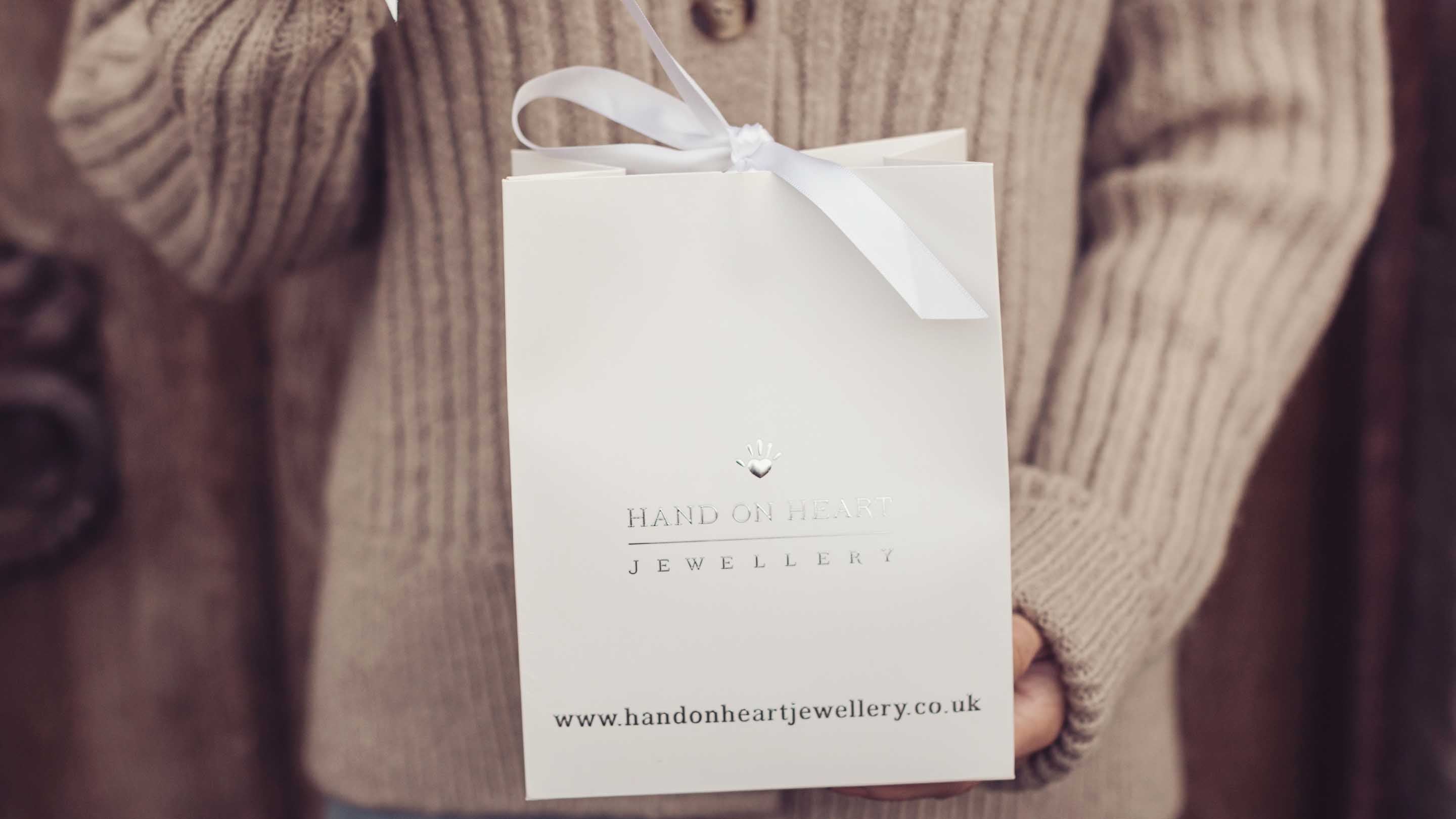 A woman in a beige cardigan untying the ribbon on a Hand on Heart Gift Bag