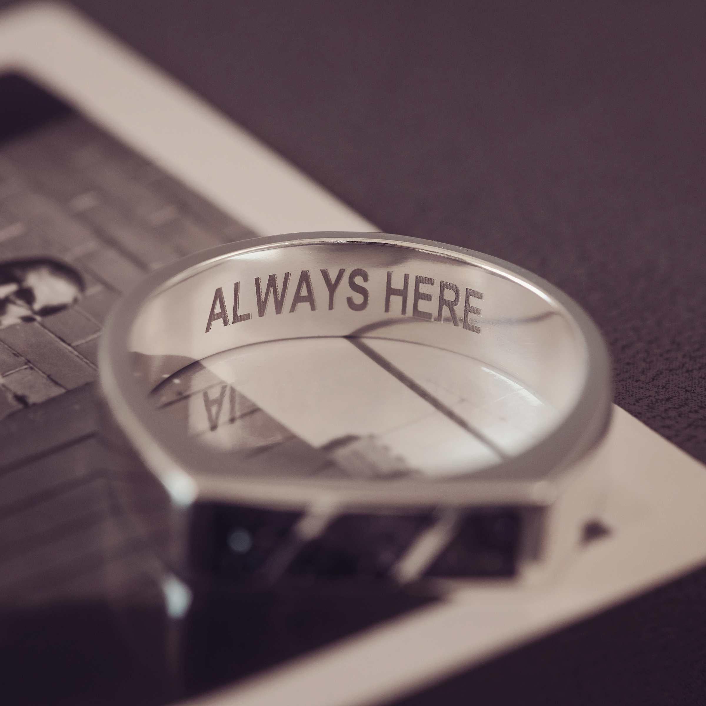 Silver ring with 'ALWAYS HERE' engraving on a blurred background