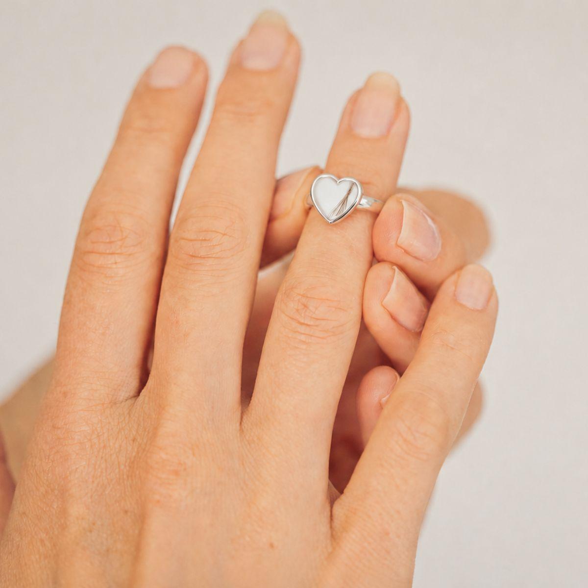 Hand wearing a silver heart-shaped ring on a plain background