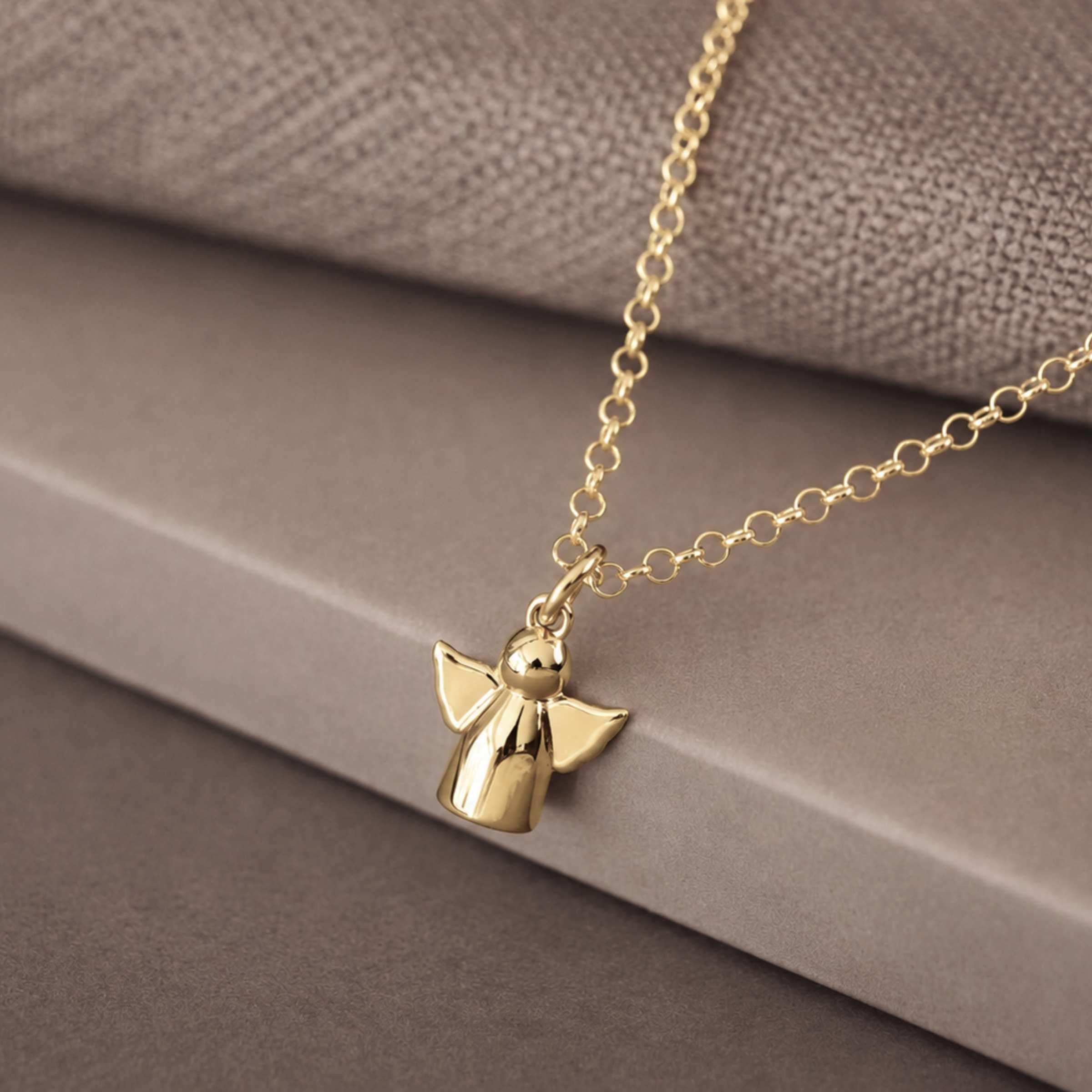 Gold pendant with chain in the shape of an angel on a brown backgound.