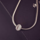 Silver thick snake chain with an oval charm on a dark background