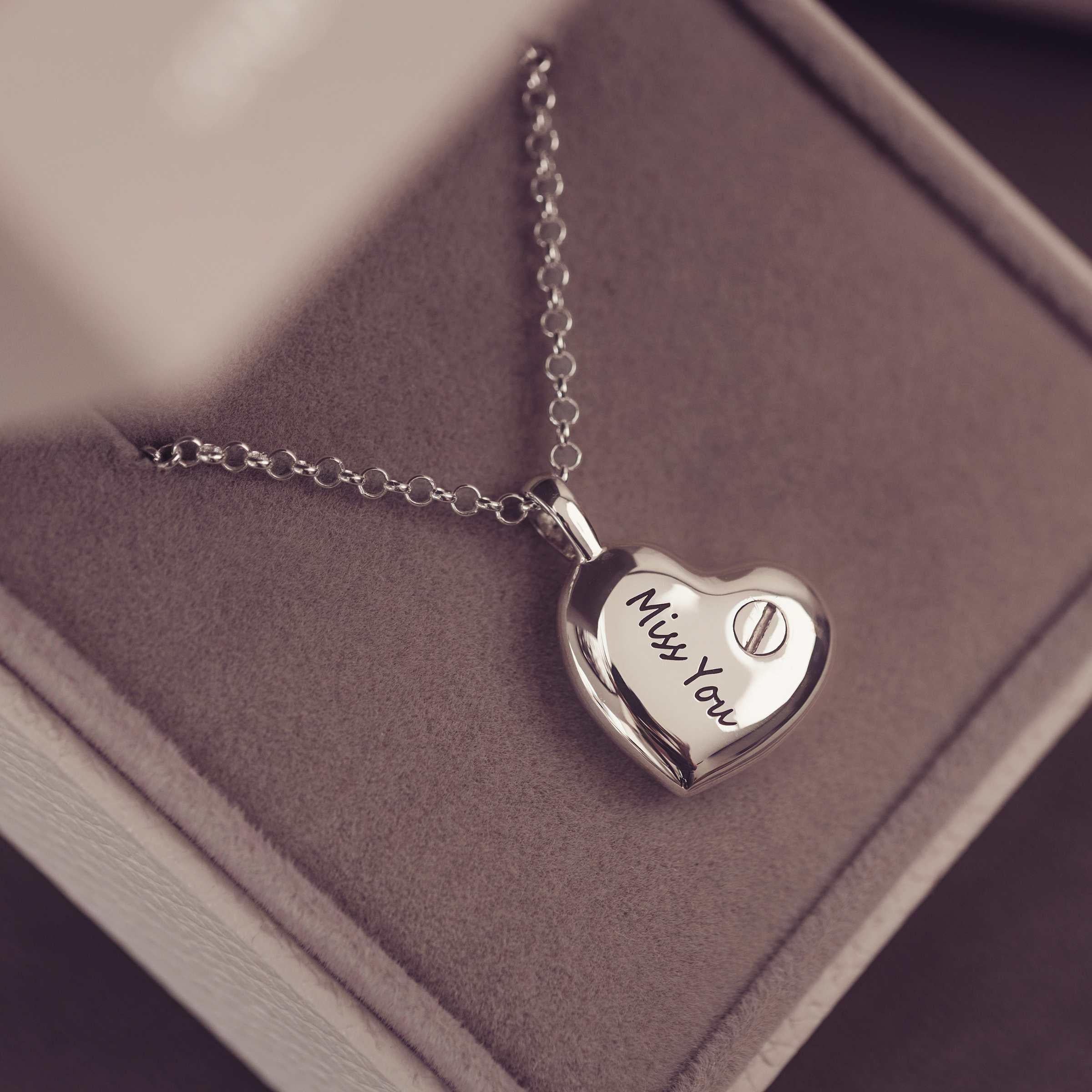 Silver heart-shaped locket with 'Miss You' engraving on a soft surface