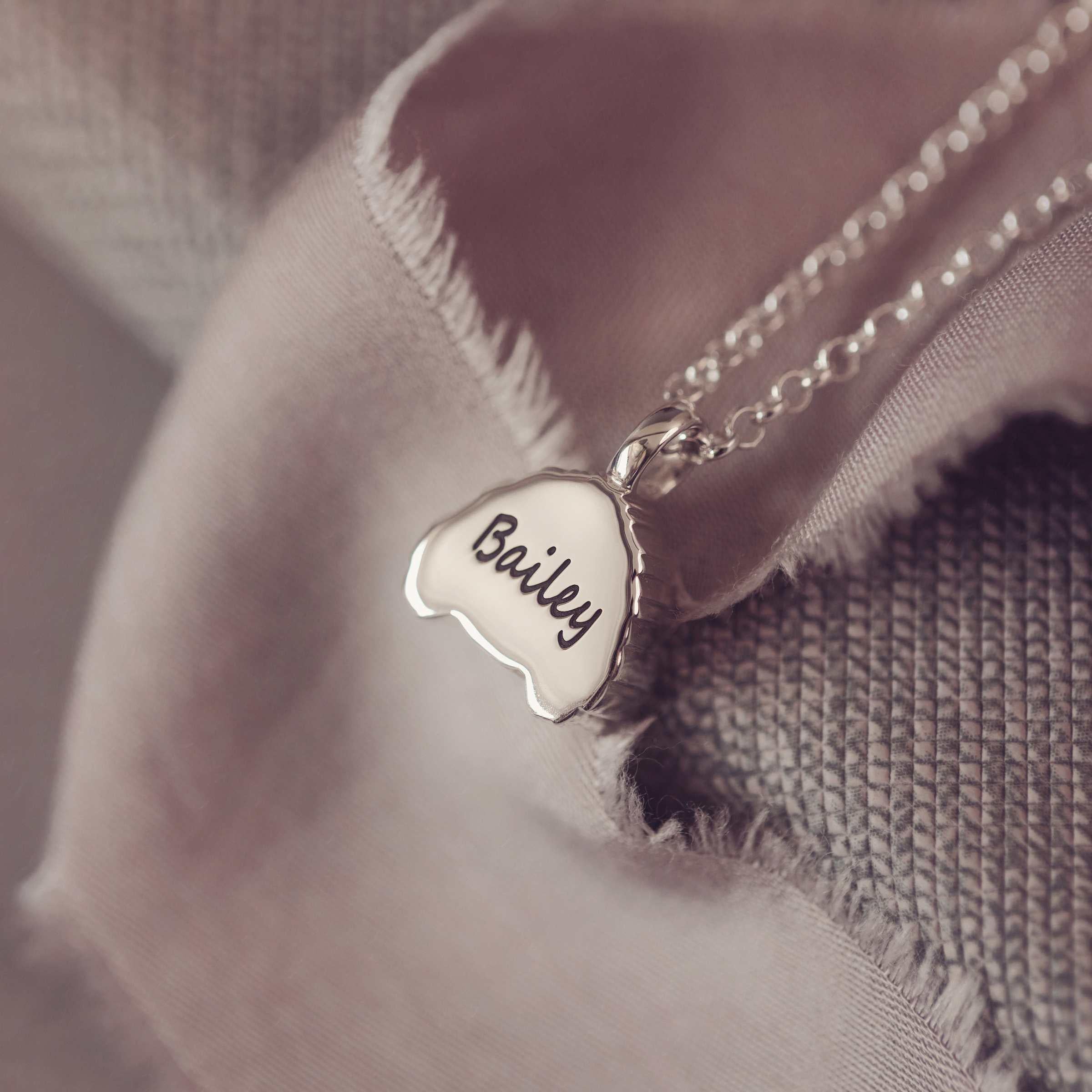 Silver necklace with a dog-shaped pendant engraved 'Bailey' on a soft fabric background