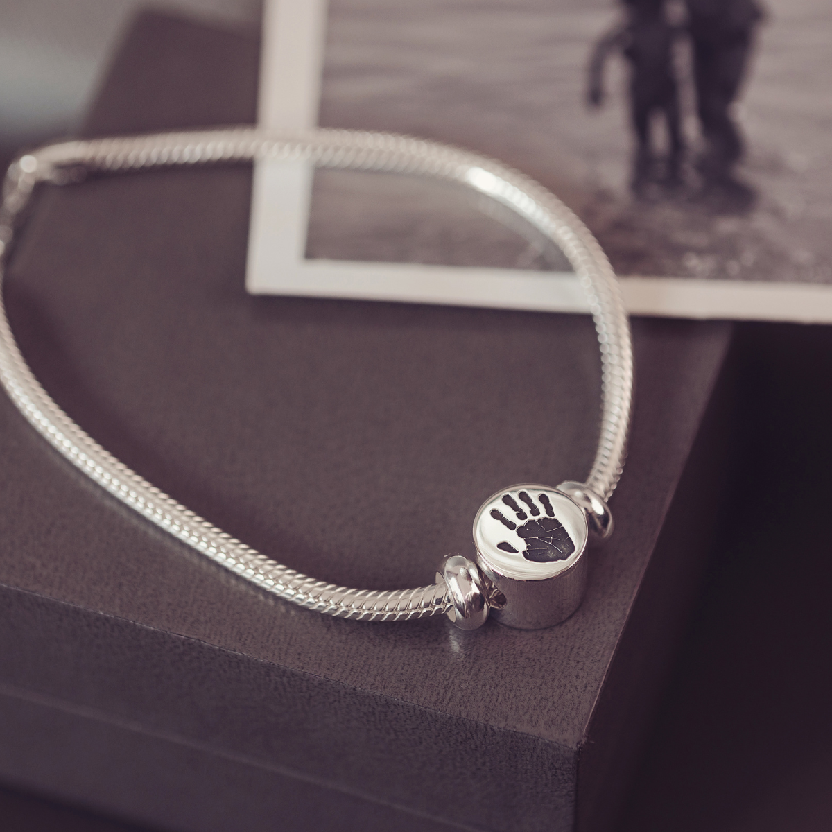Silver bracelet with a handprint charm on a dark surface