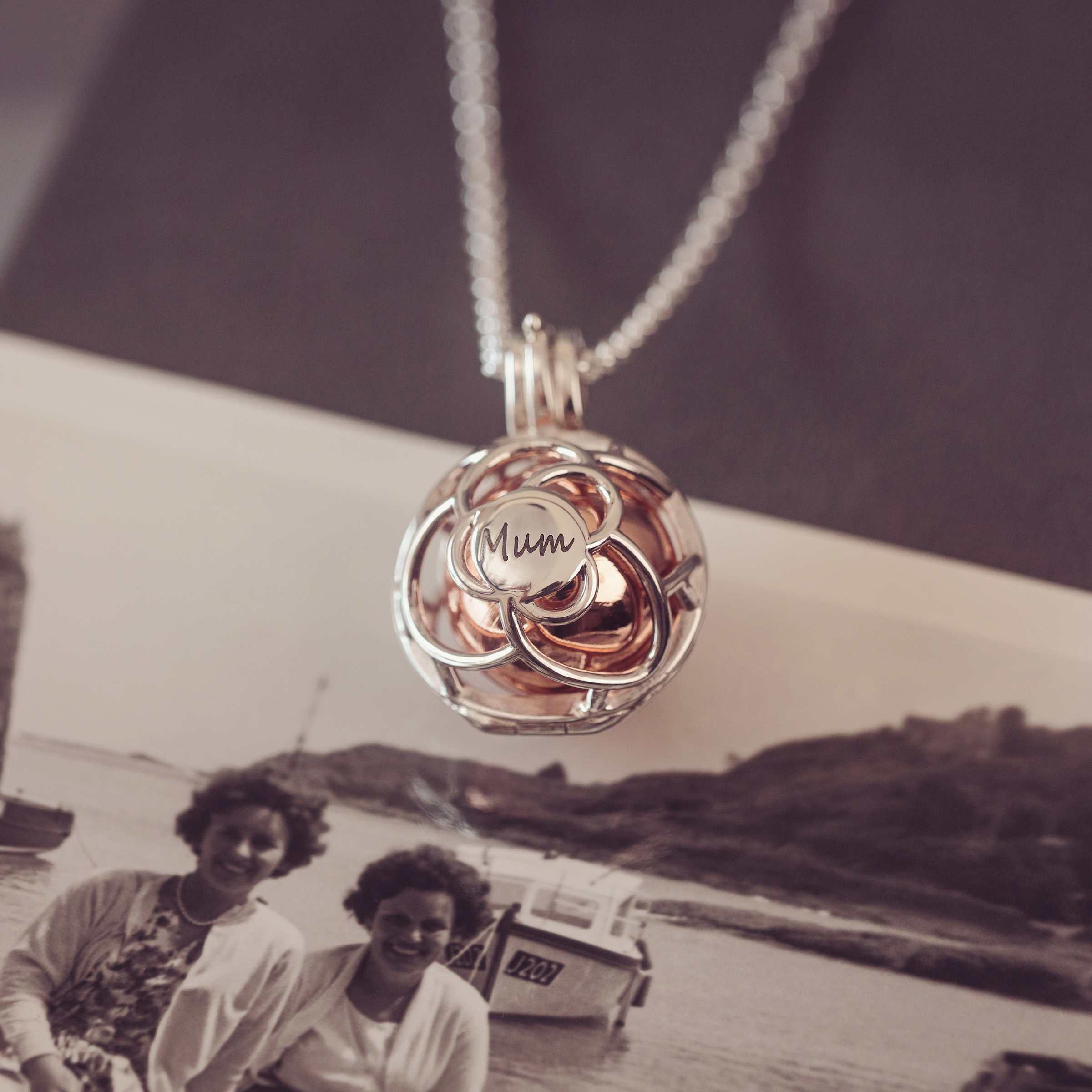 Silver and Rose gold pendant with 'Mum' engraving on a chain, over an old photograph of two women by a boat.