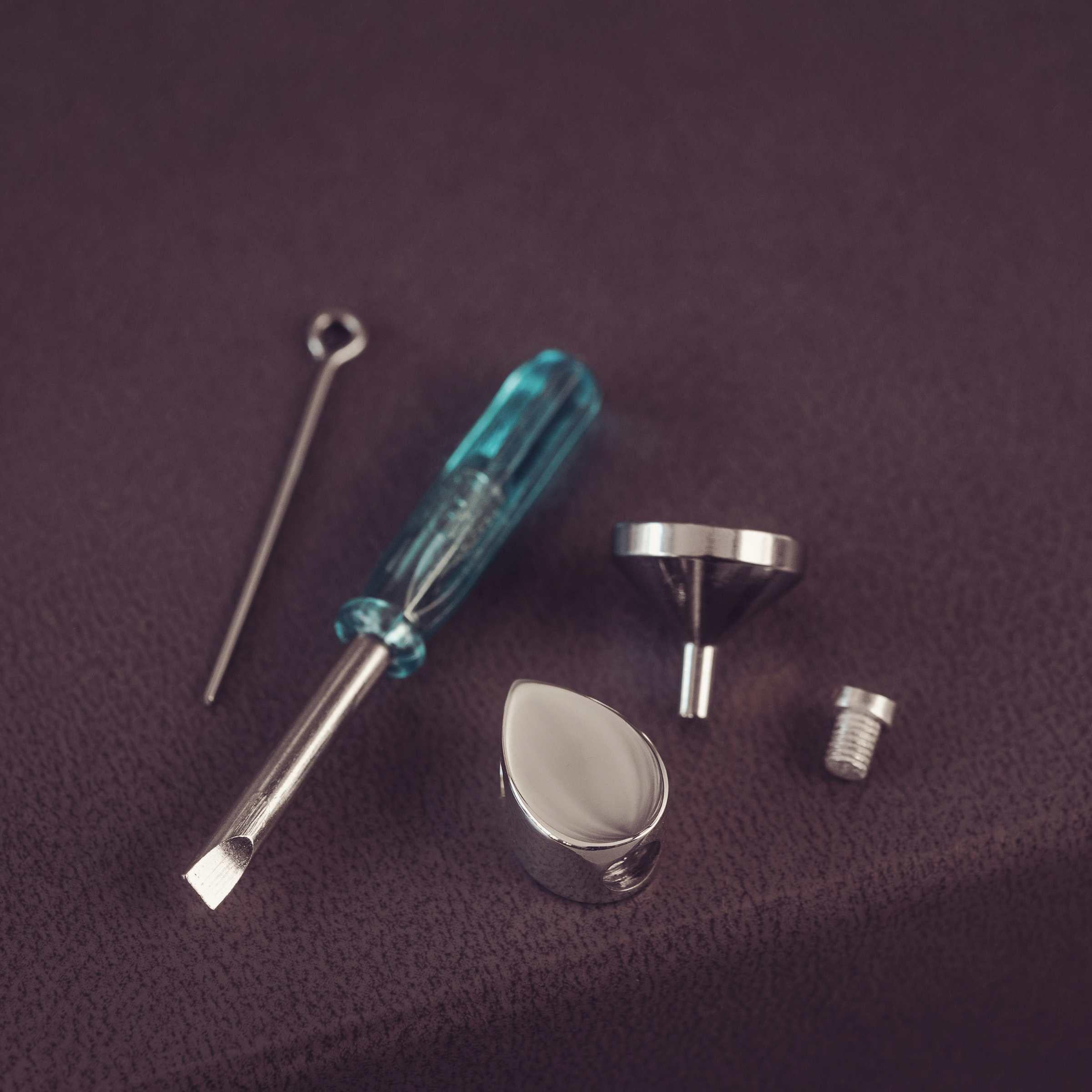 Set of small tools including a screwdriver, funnel, and other metallic items on a purple fabric background