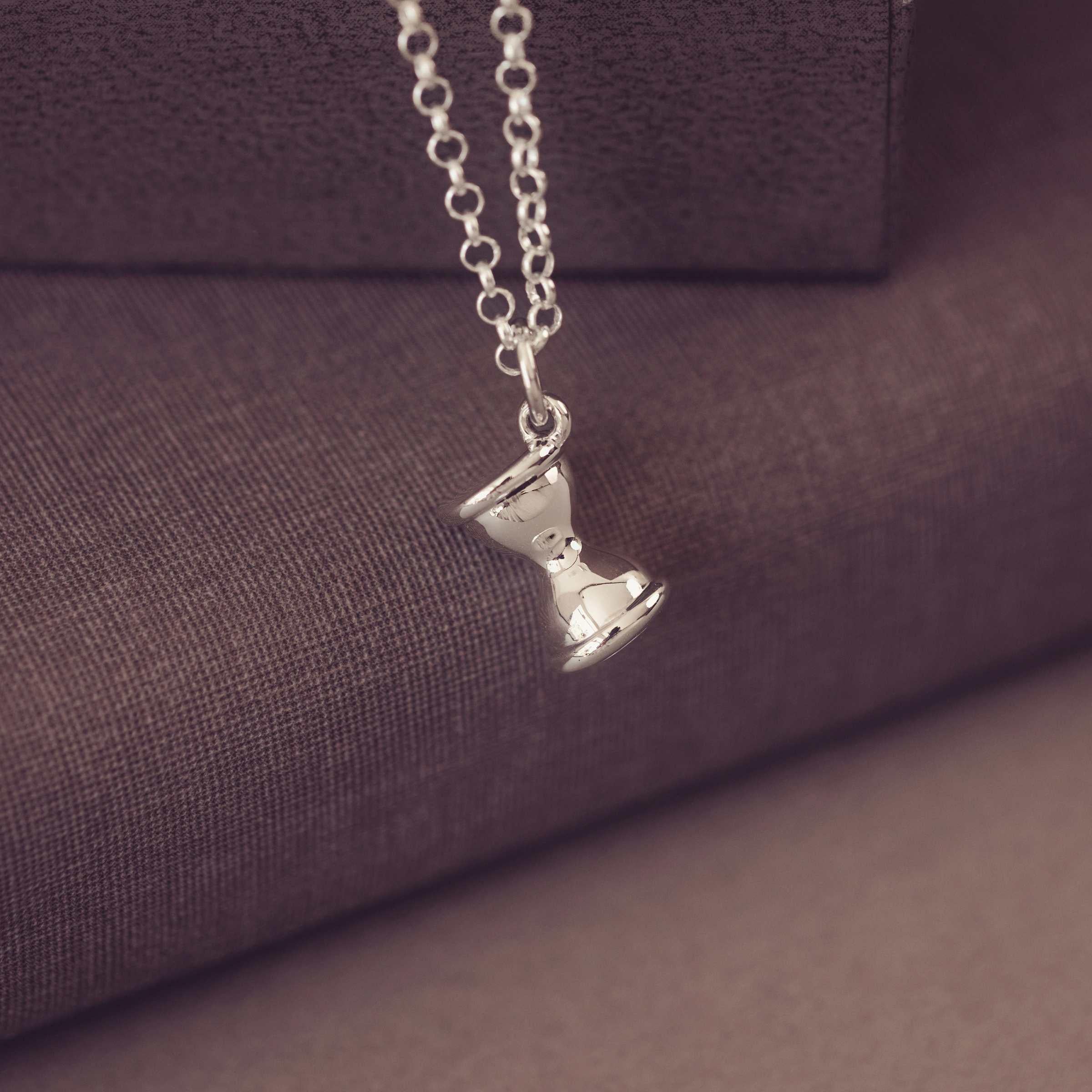 Silver necklace with a hourglass pendant on a purple fabric background