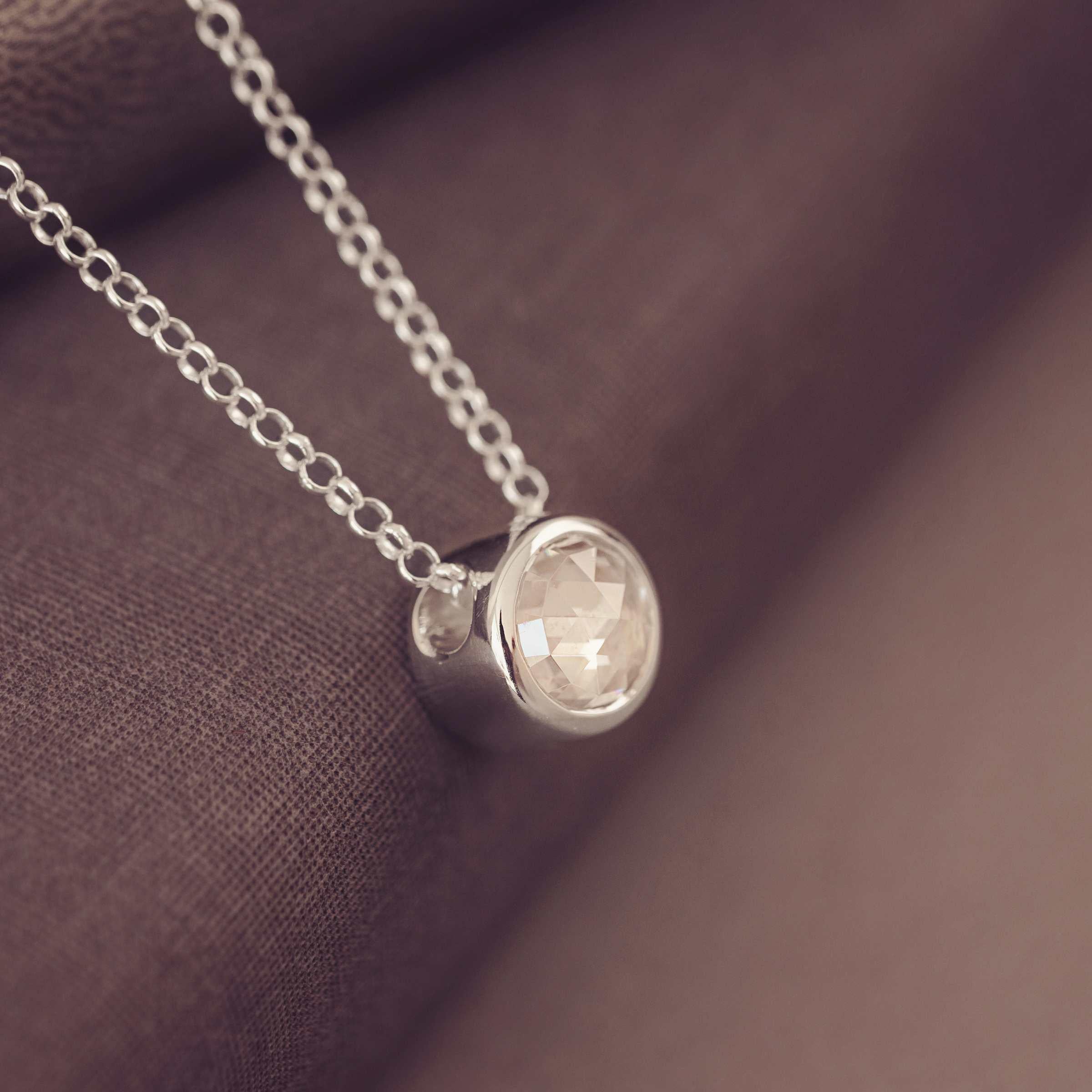 Silver necklace  with a round gemtstone pendant on a brown fabric background