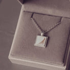 Silver necklace with a square pendant on a gray textured surface