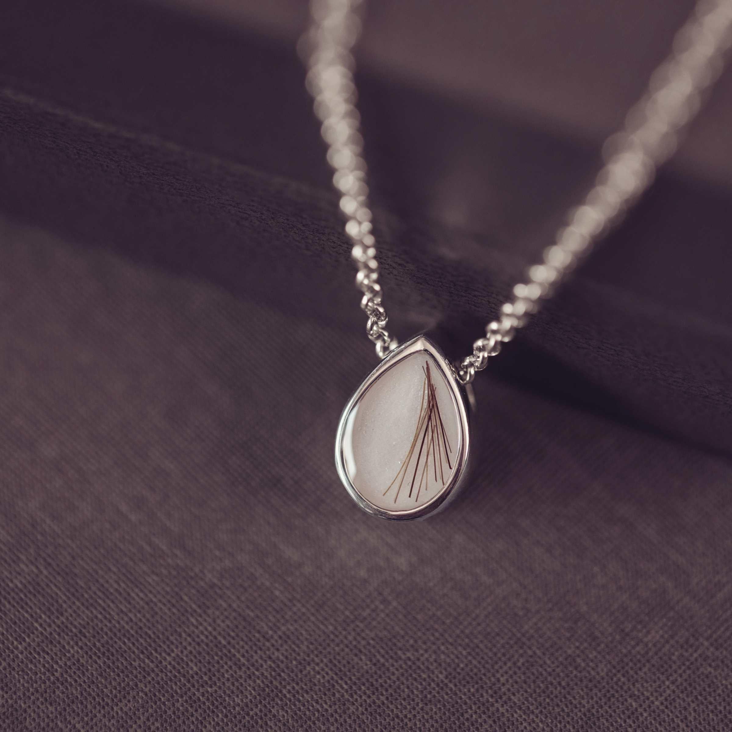 silver teardrop shaped pendant on a dark background