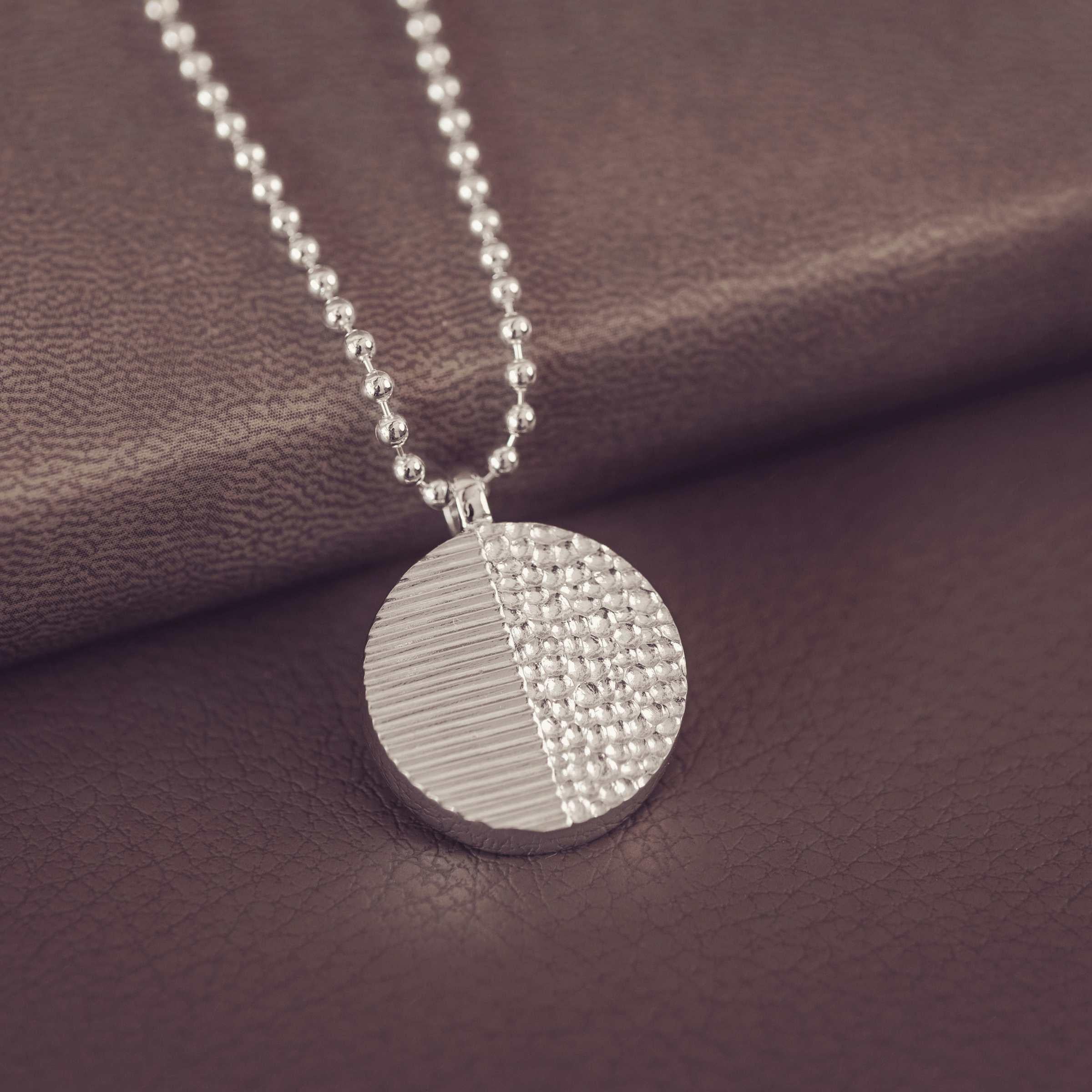 Silver necklace with a textured pendant on a brown fabric background