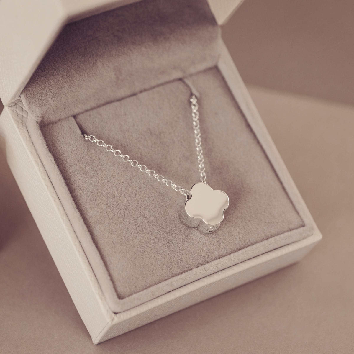 Silver necklace with a clover-shaped pendant in an open jewelry box.