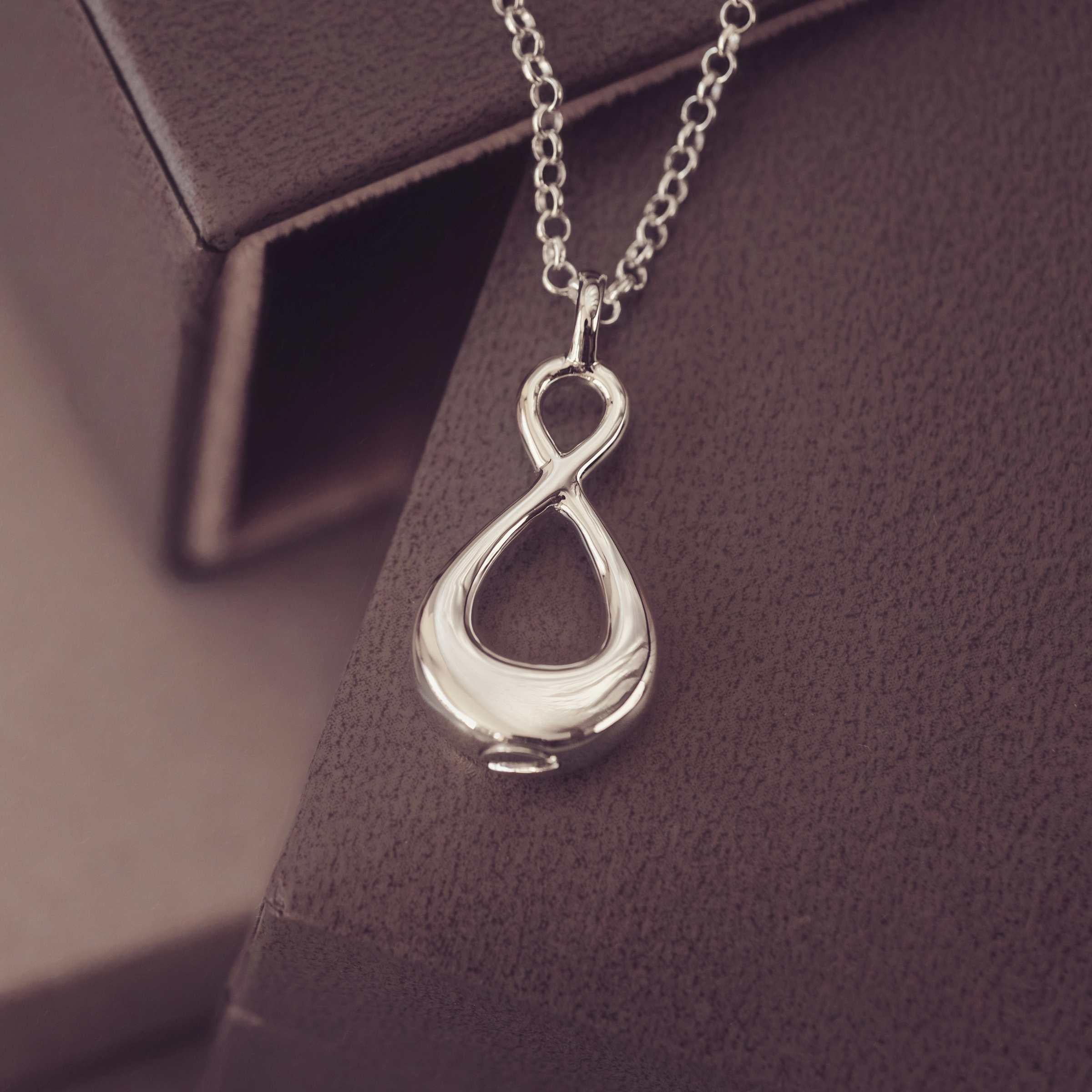 Silver infinity pendant necklace on a dark textured surface