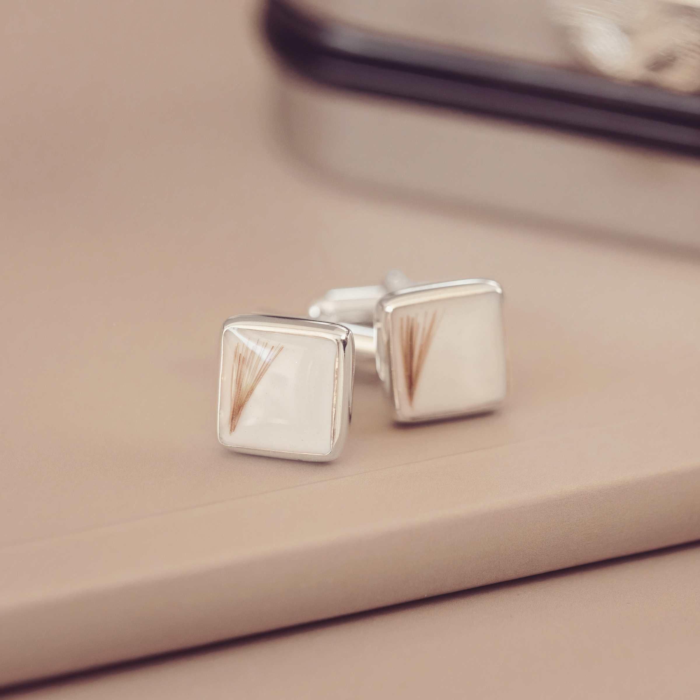 Silver square cufflinks on a beige surface