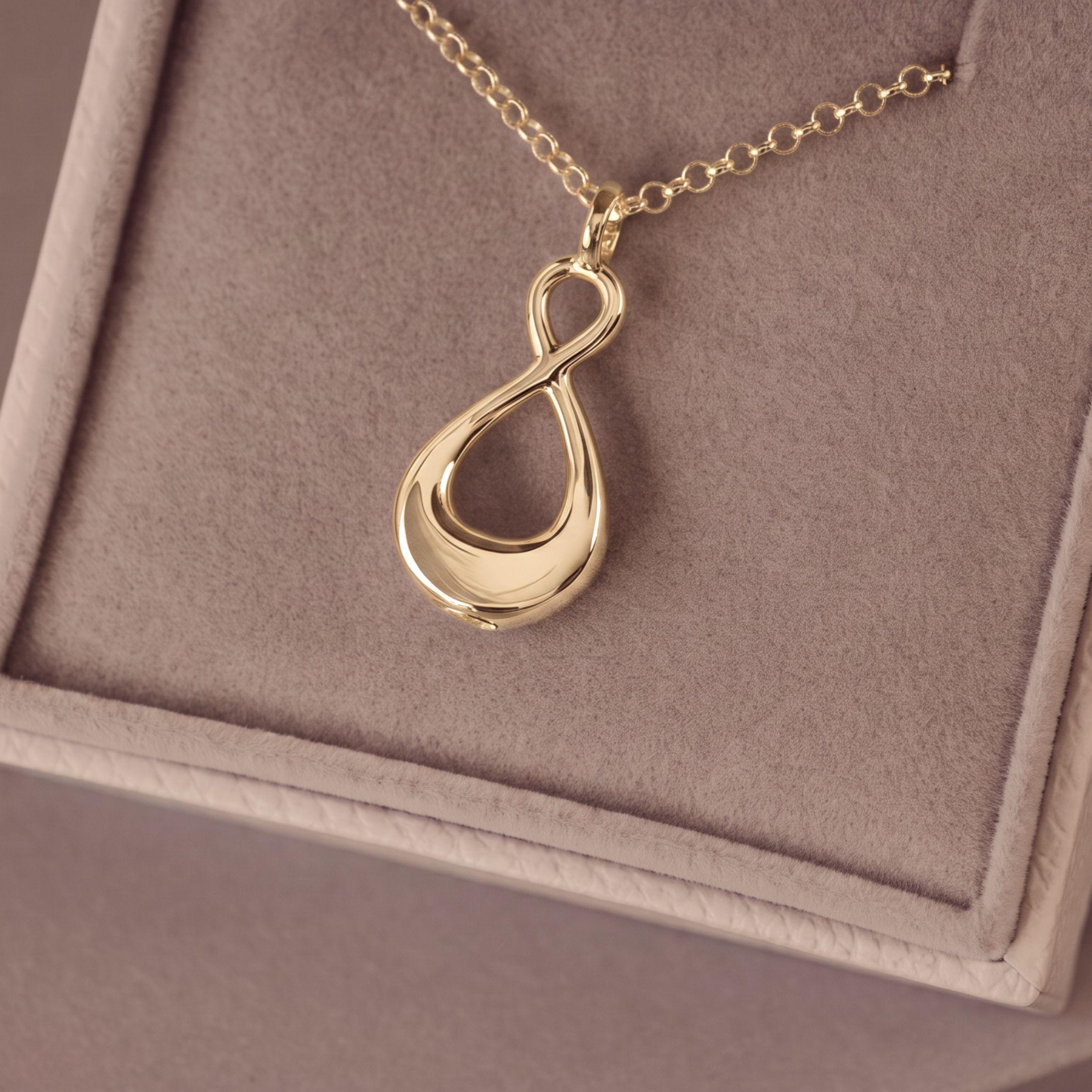 A gold infinity pendant necklace resting on a soft beige jewelry box.