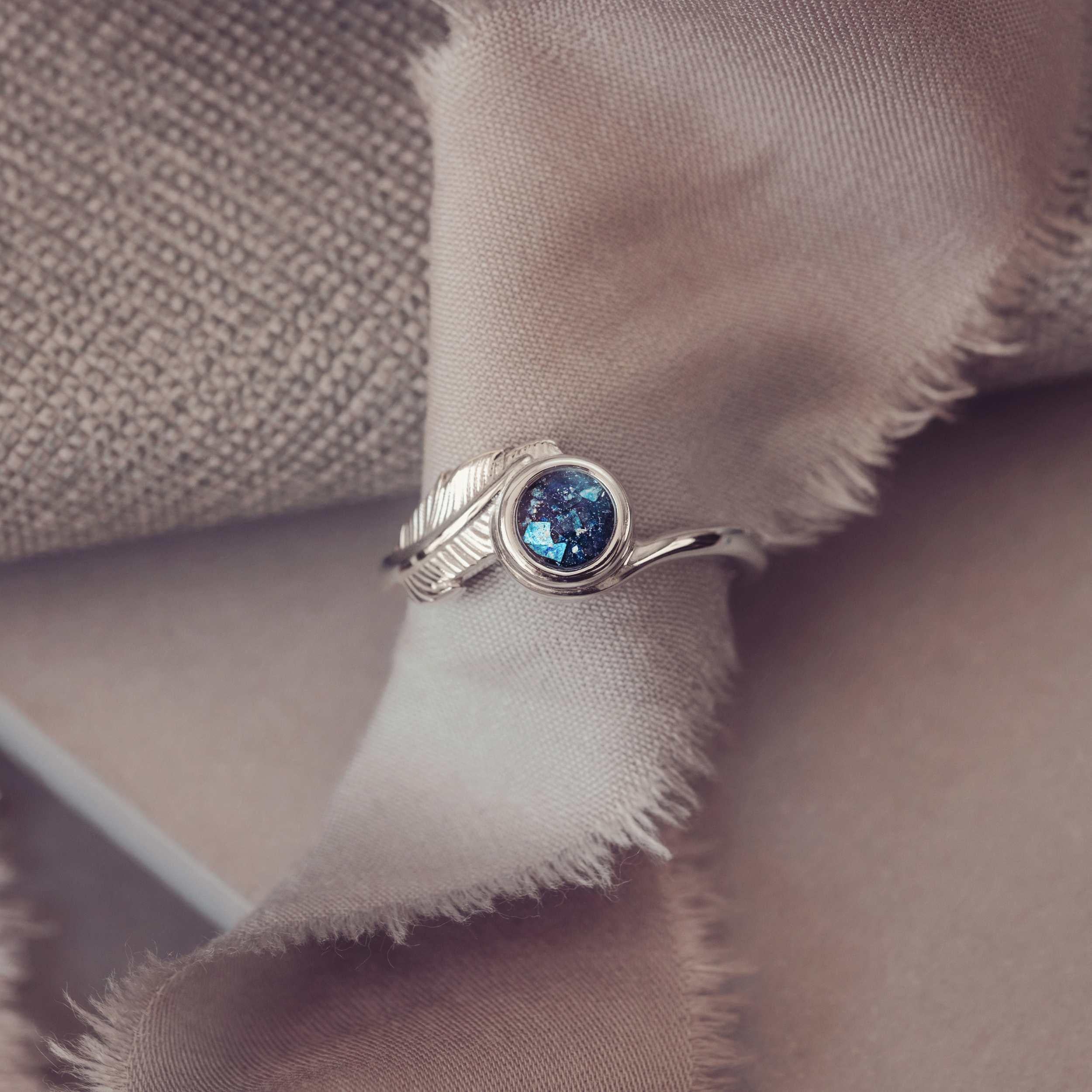 A silver ash filled feather ring sitting around a piece of cloth on a neutral backgound.