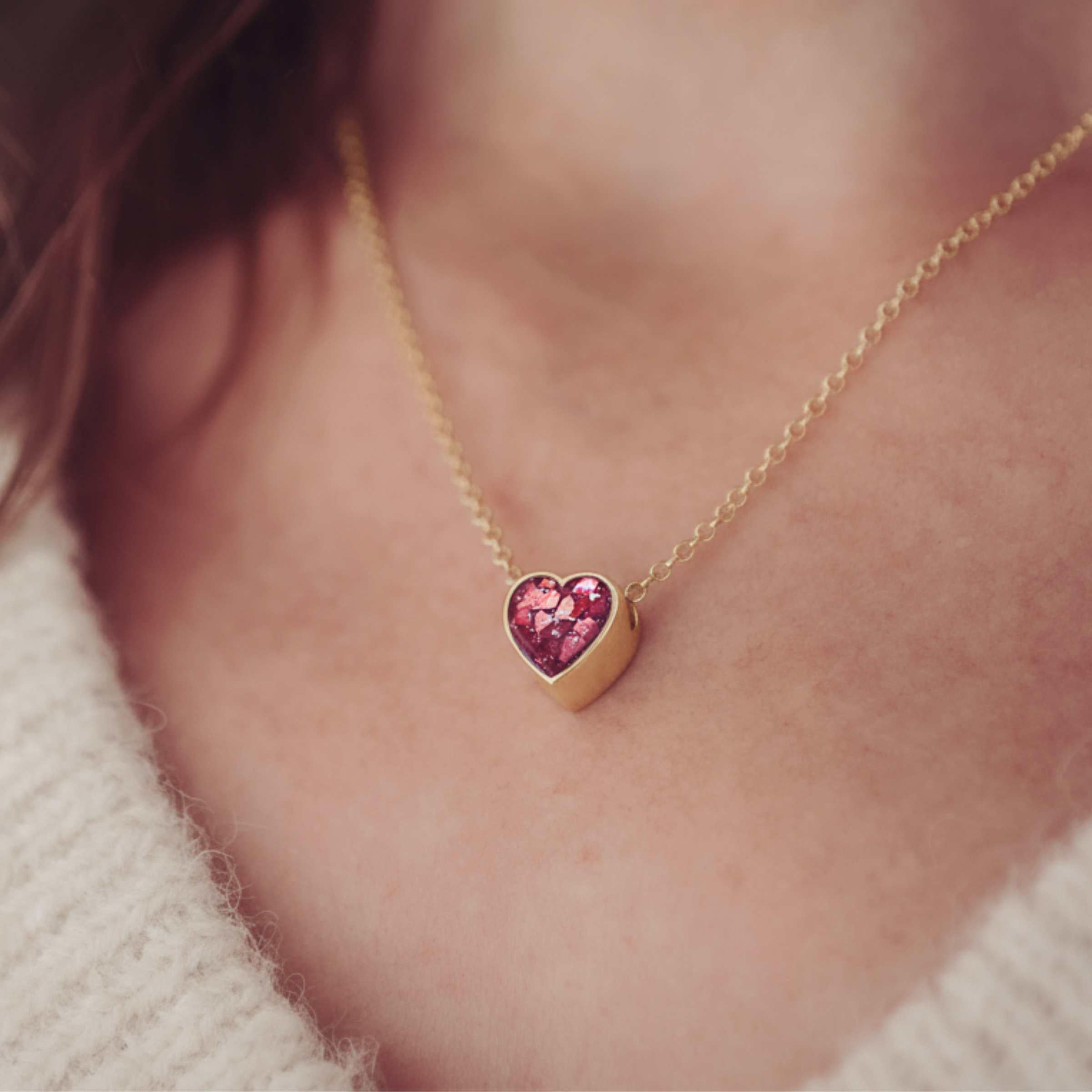 Gold necklace with a heart-shaped resin pendant worn by a person.