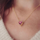 Gold necklace with a heart-shaped resin pendant worn by a person.