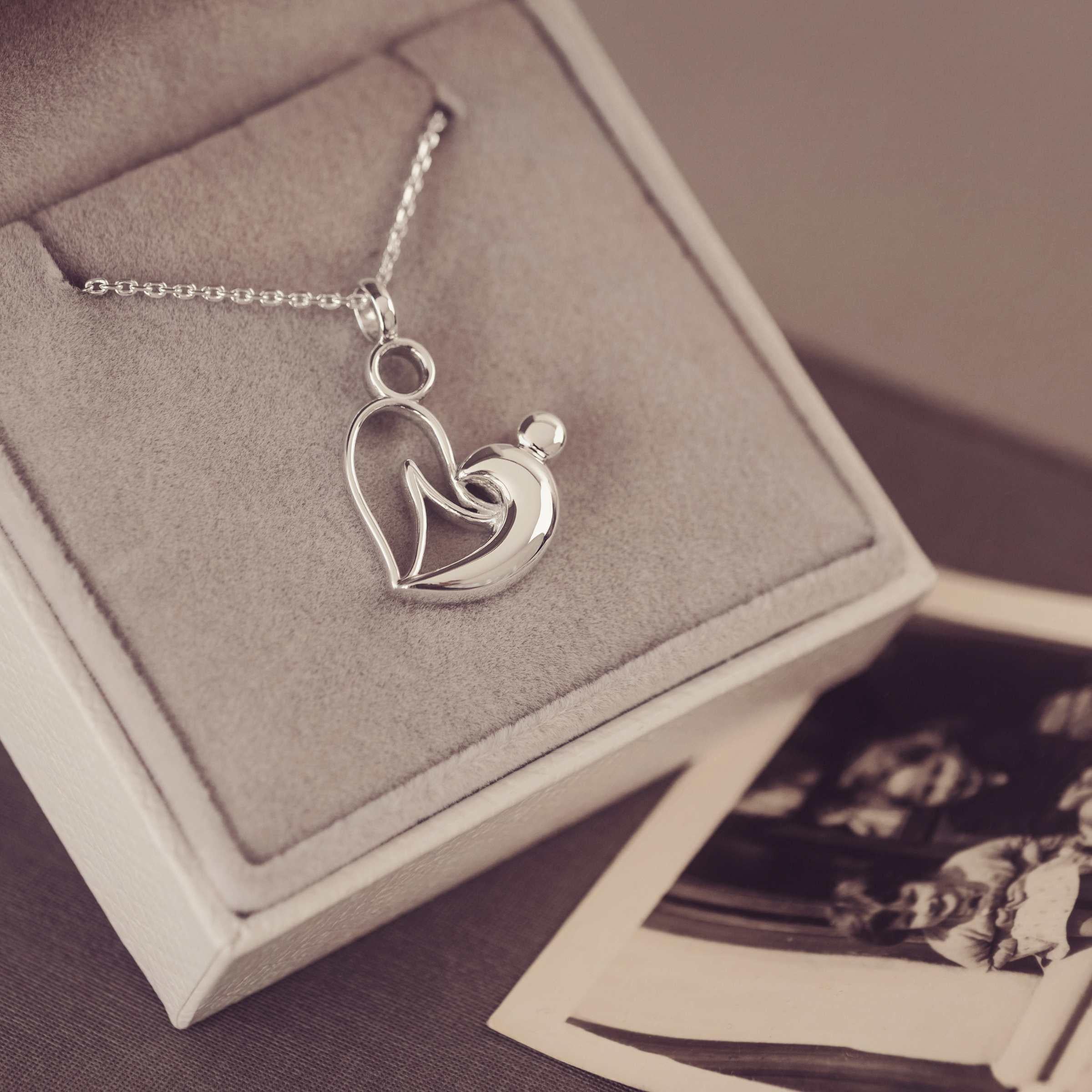 Silver necklace with two person heart pendant in a jewellery box with vintage photos.