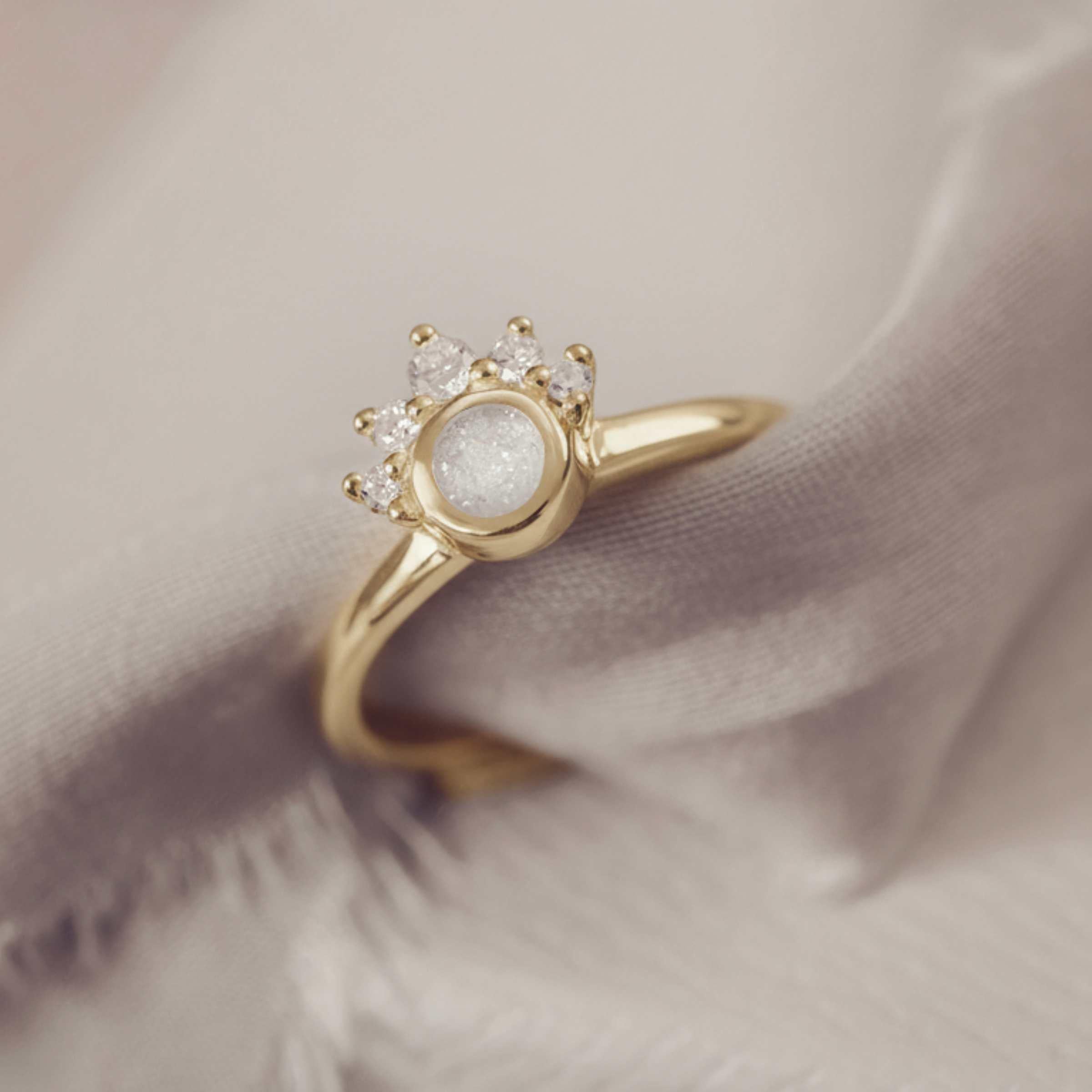 Gold cluster ring with a white sparkle resin and smaller stones on a soft fabric background