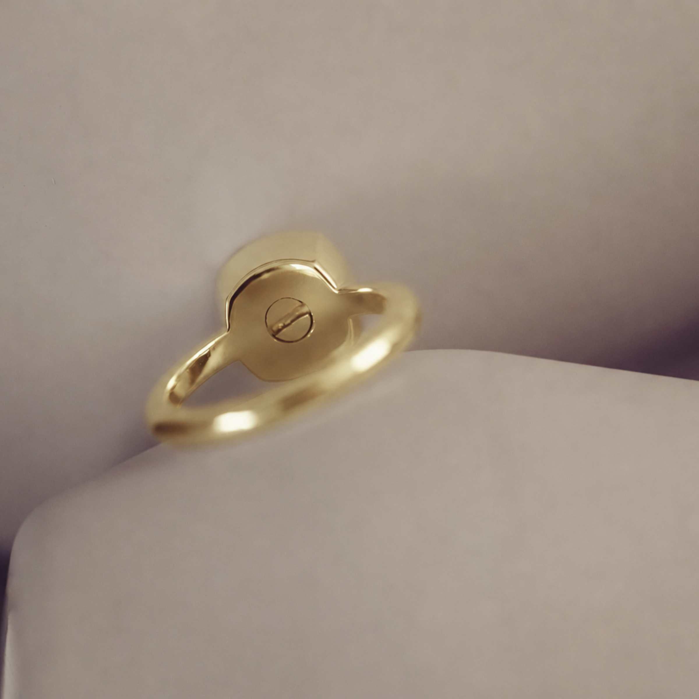 Gold ring showing a screw on a cream background