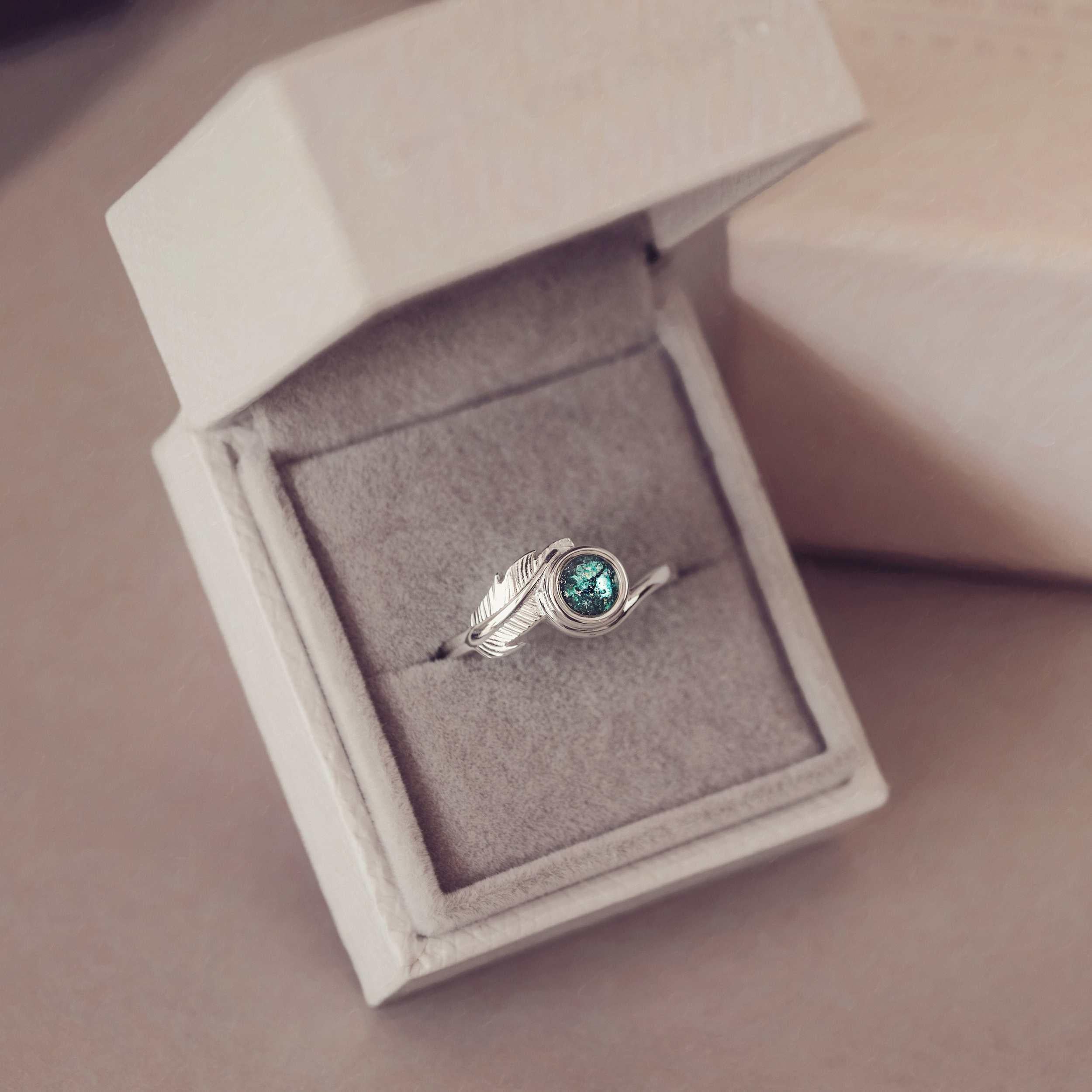 A silver ash filled feather ring in a jewellery box