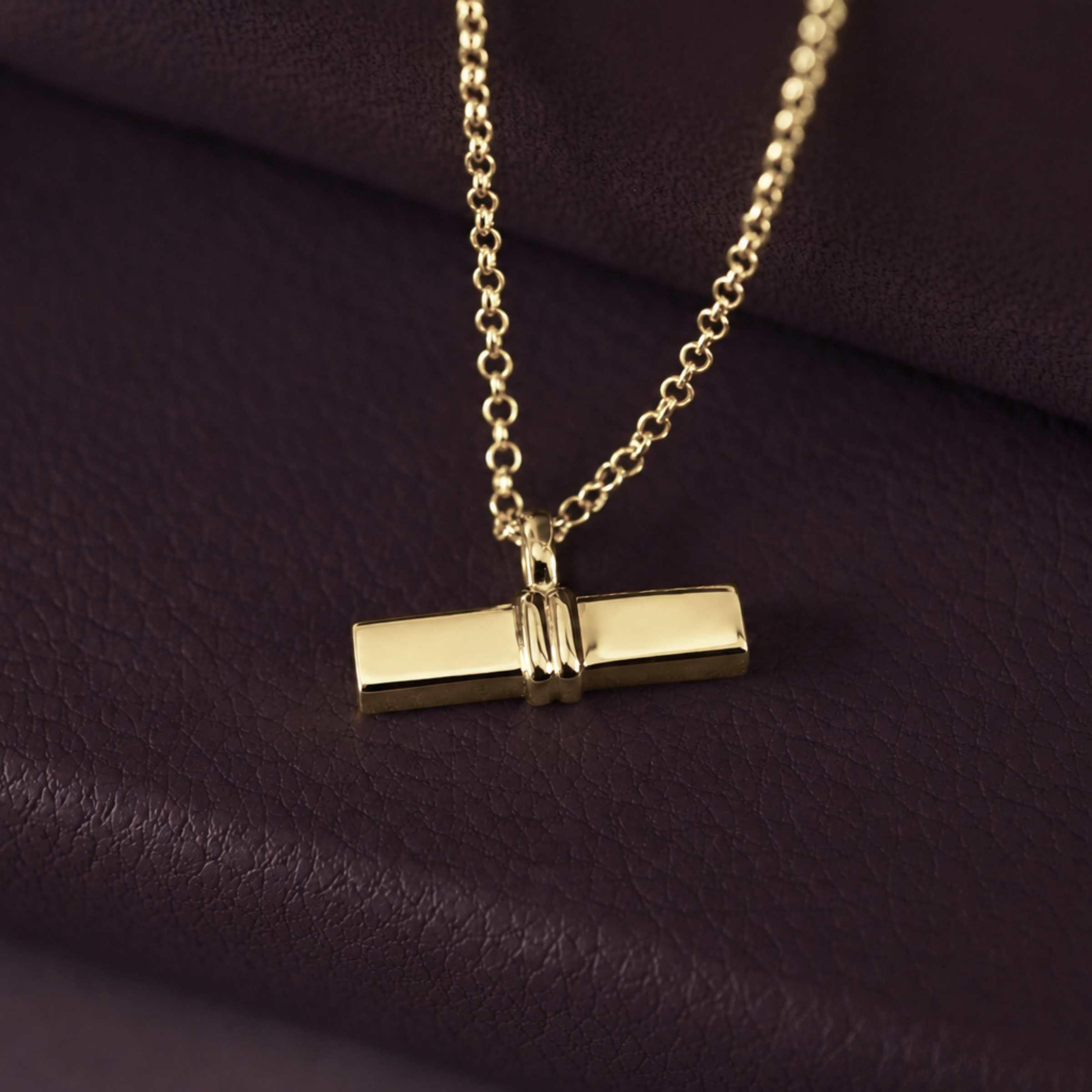 Gold T Bar necklace with a pendant on a dark purple fabric background