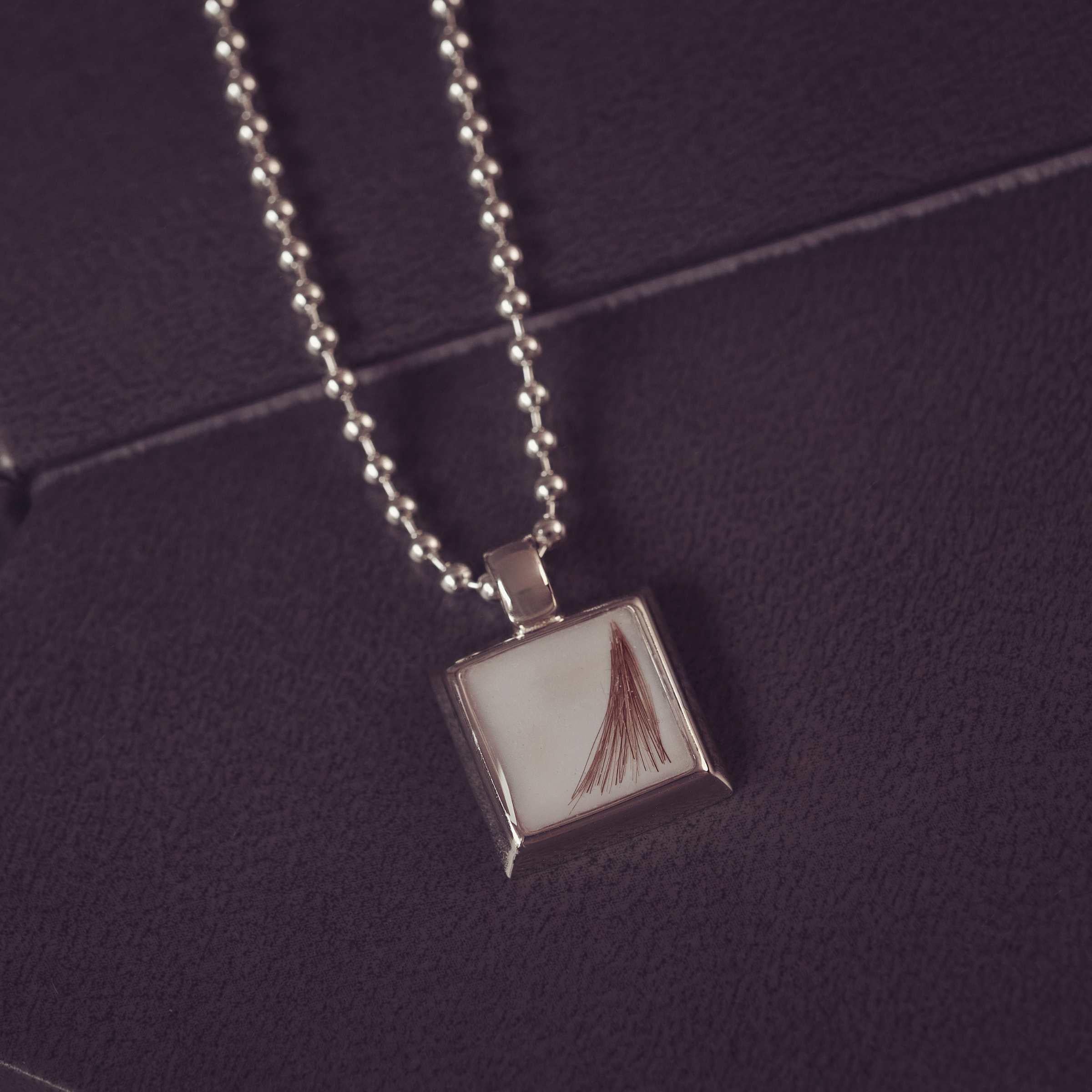 Silver necklace with a square pendant on a dark purple background