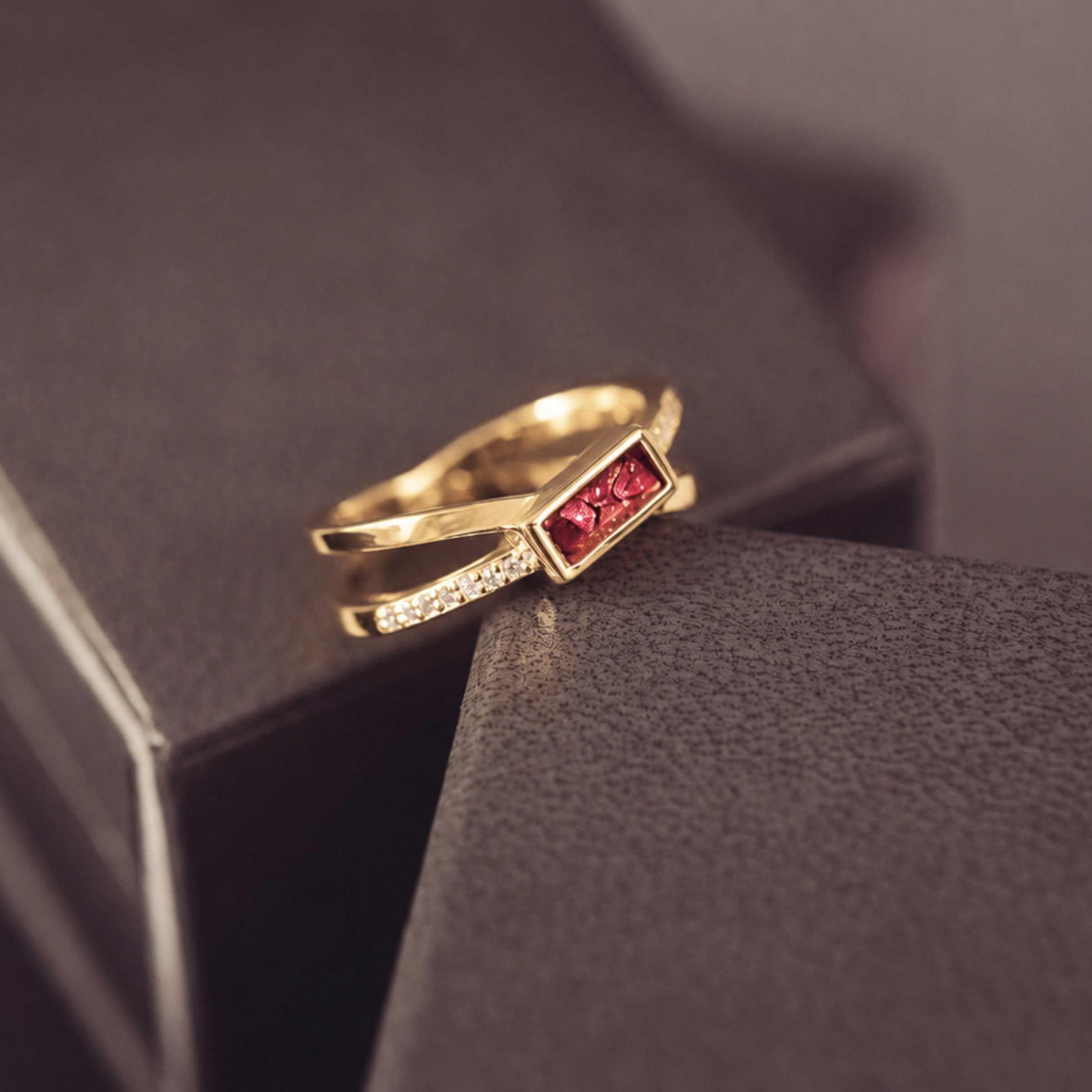 gold criss cross ring with a red rectangle ash stone and gemstones on a dark background